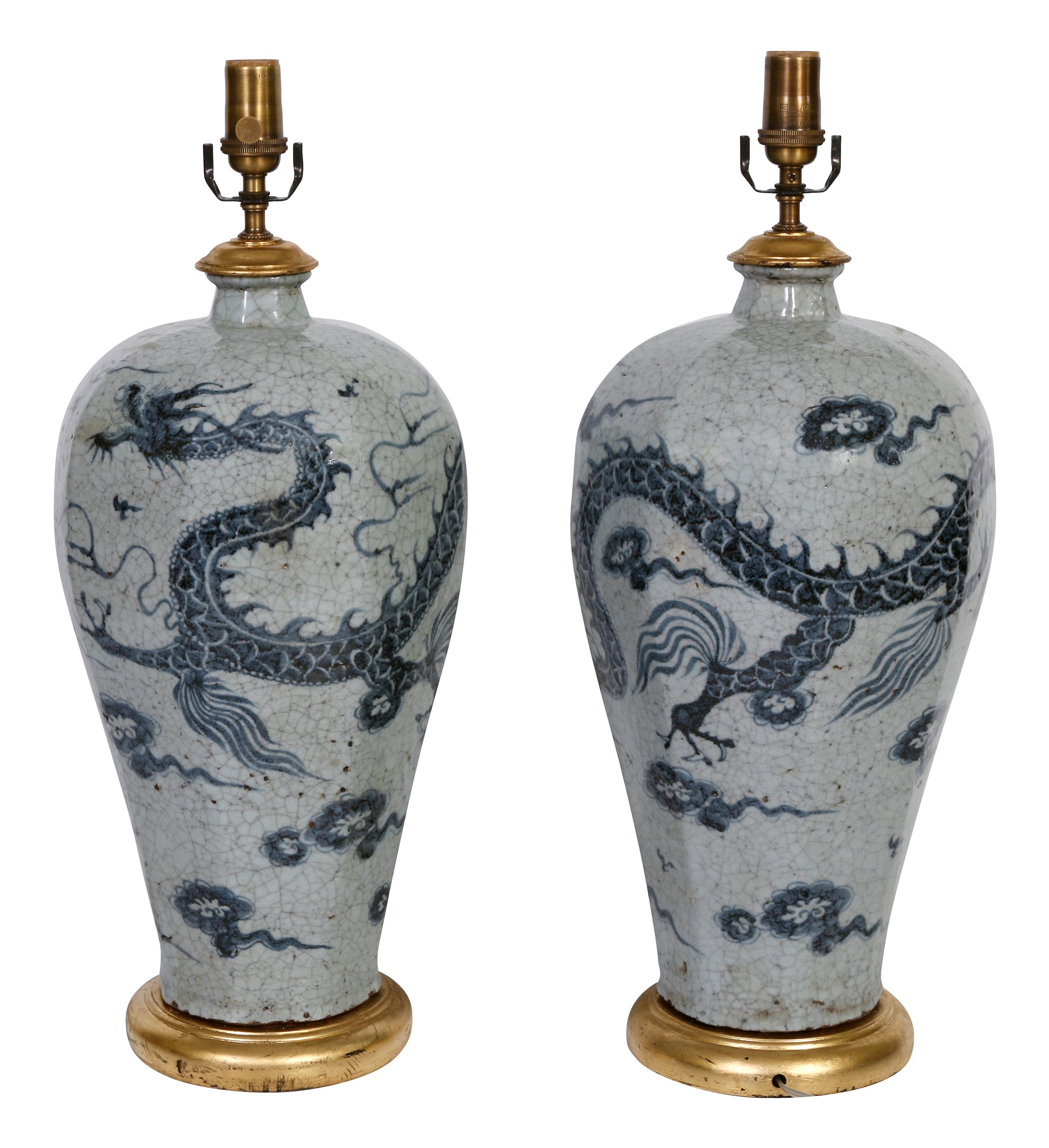 A great looking pair of Chinese export lamps in a blue/gray. crackle glaze with a dragon motif. The lamps are mounted on a giltwood base and are topped with off-white box-pleated shades.