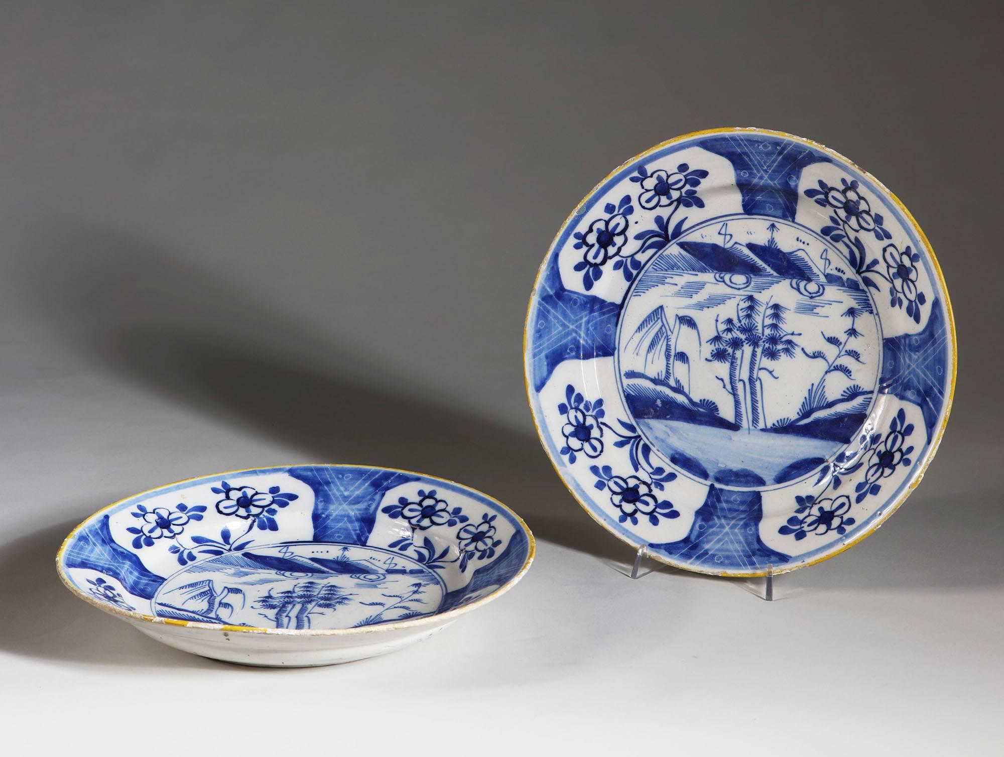 A pair of mid-18th century blue and white English Delft chargers, with contrasting yellow rims, portraying exotic trees in a landscape.