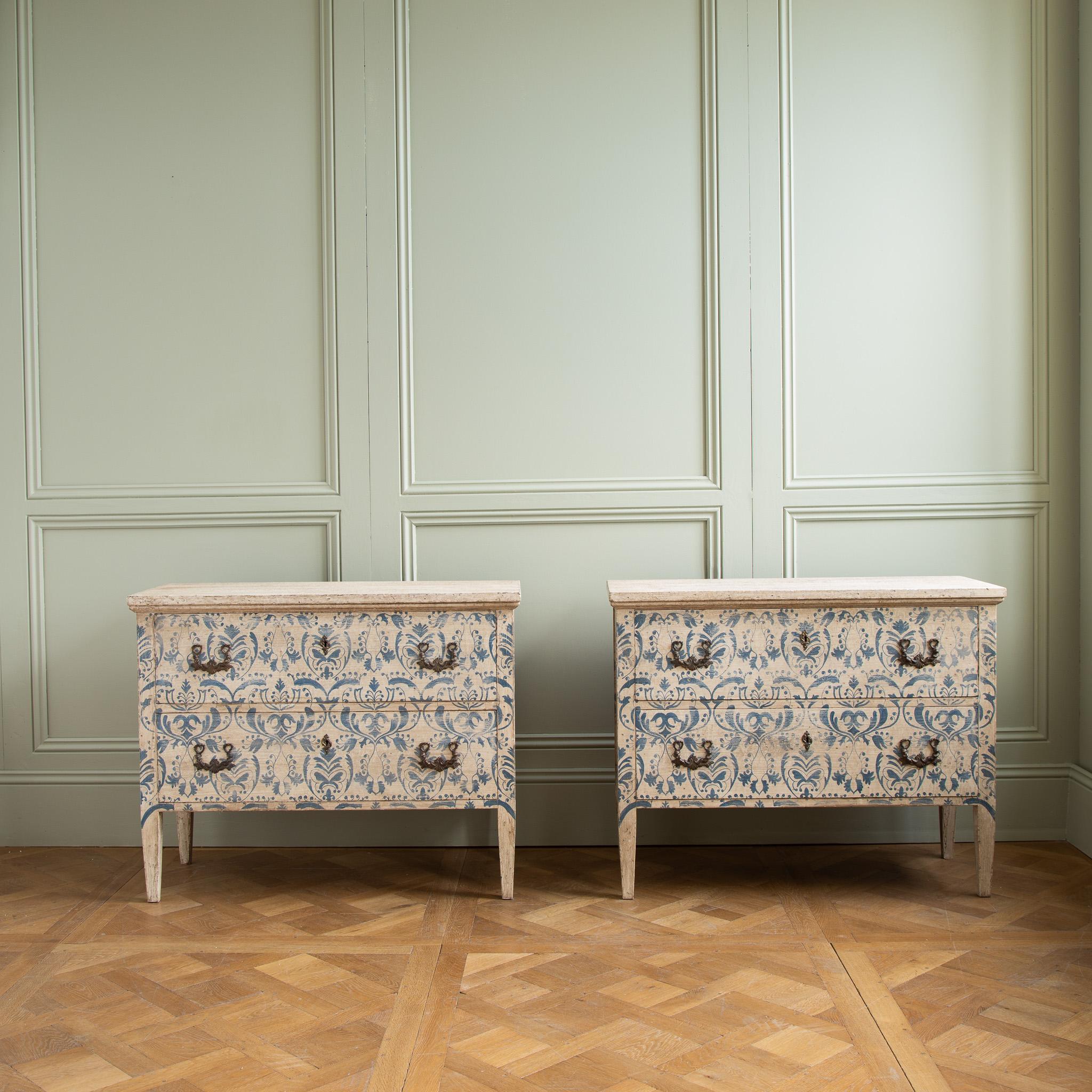 A vivid pair of Italian chests of drawers, hand painted in the traditional Florentine style featuring an aged Indigo Blue, flora and foliage motif on a background of antique white. The motif covers the front and both sides of the body. The paint