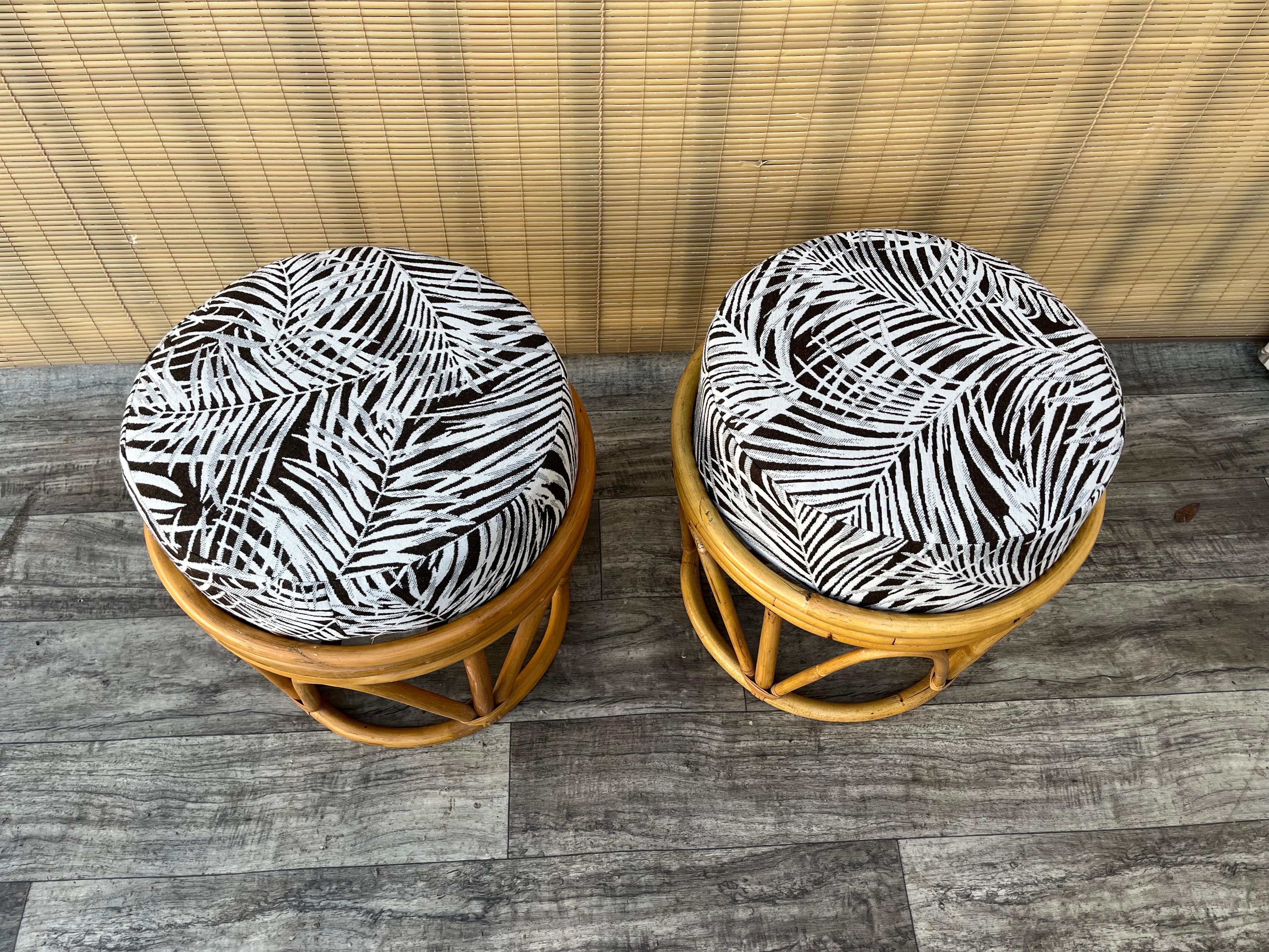 Ein Paar Vintage Bohemian Coastal Style  Rattan-Fußhocker / Ottomane. Circa 1980er Jahre
Mit gebogenen Rattanrahmen und abnehmbaren runden Kissen.
In ausgezeichnetem Originalzustand mit sehr geringen Gebrauchs- und Altersspuren. Das Kissen wurde vor
