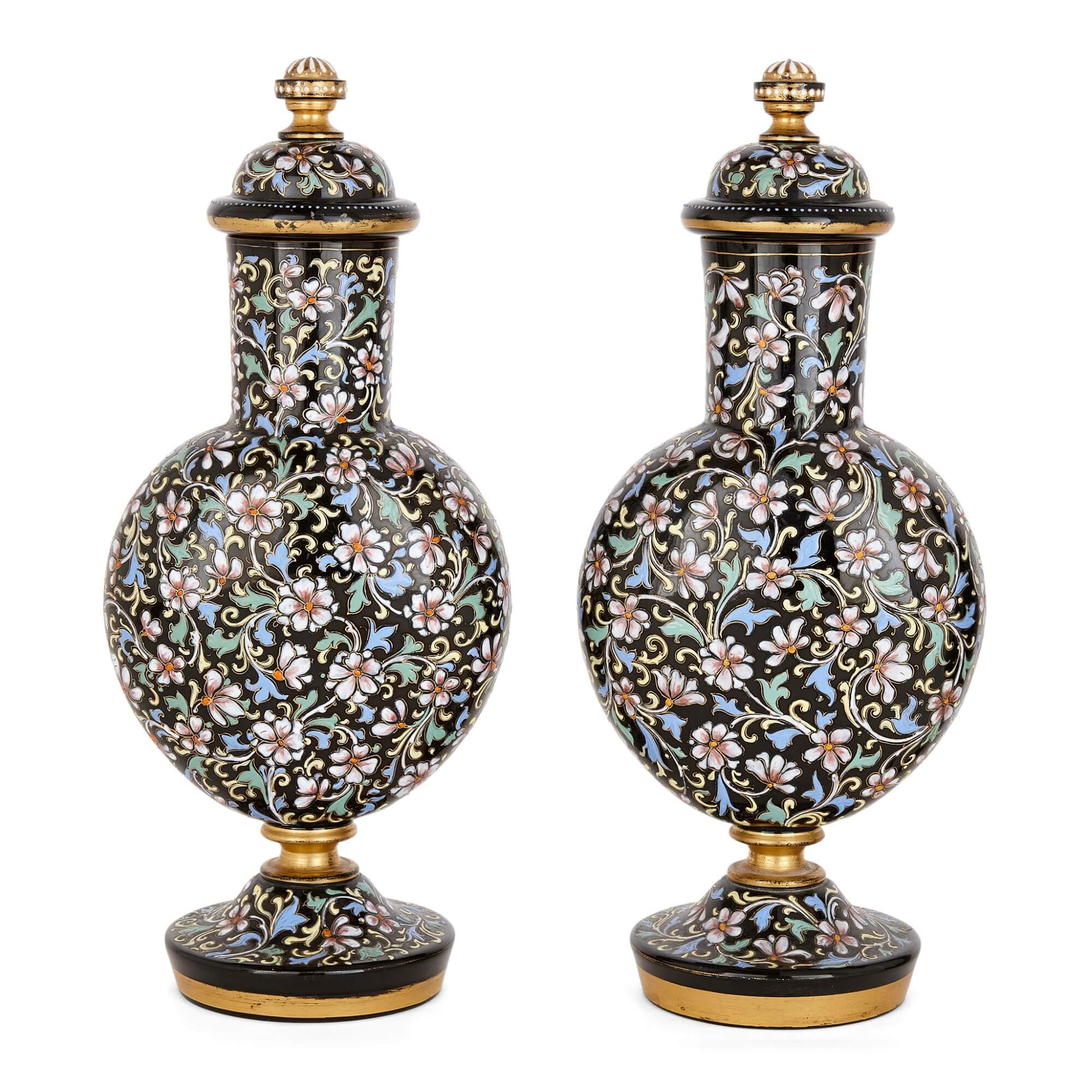 A pair of Bohemian enamelled black glass vases and covers
Bohemian, Late 19th century
Measures: Height 37cm, width 16cm, depth 12cm

Beautifully decorated with intricate floral motifs in pale pastel tones, these charming vases were made in late