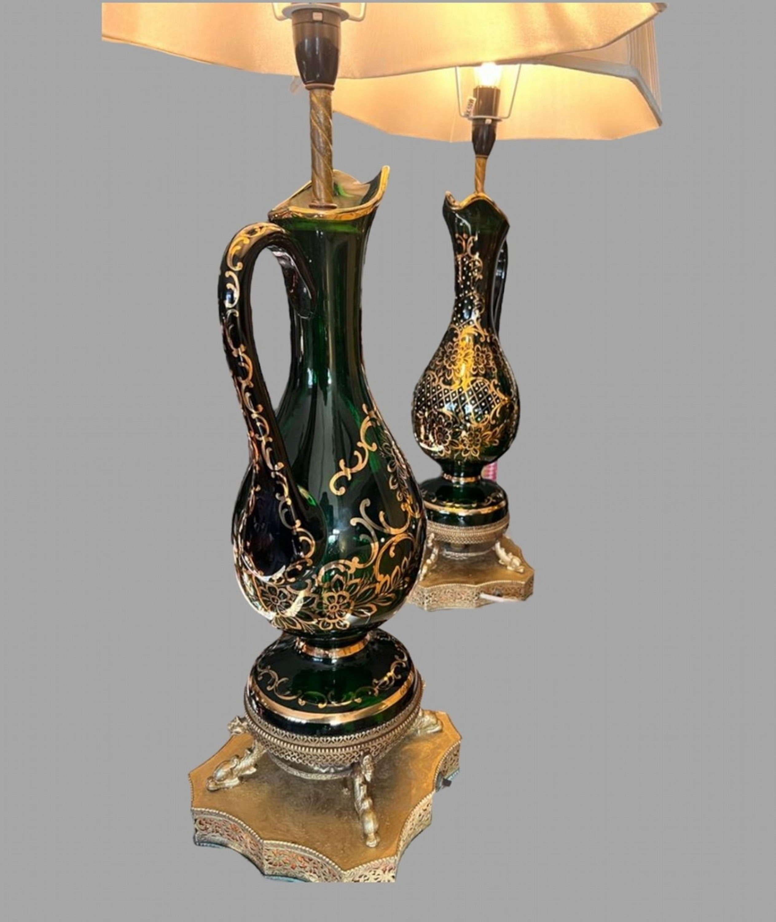 A Pair of Attractive Mid Century Bohemian Green Glass Claret Jug Lamps. Gilt pierced base with internal light. The jugs have elegant carved handles. Rewired and Pat tested. Shades not included.