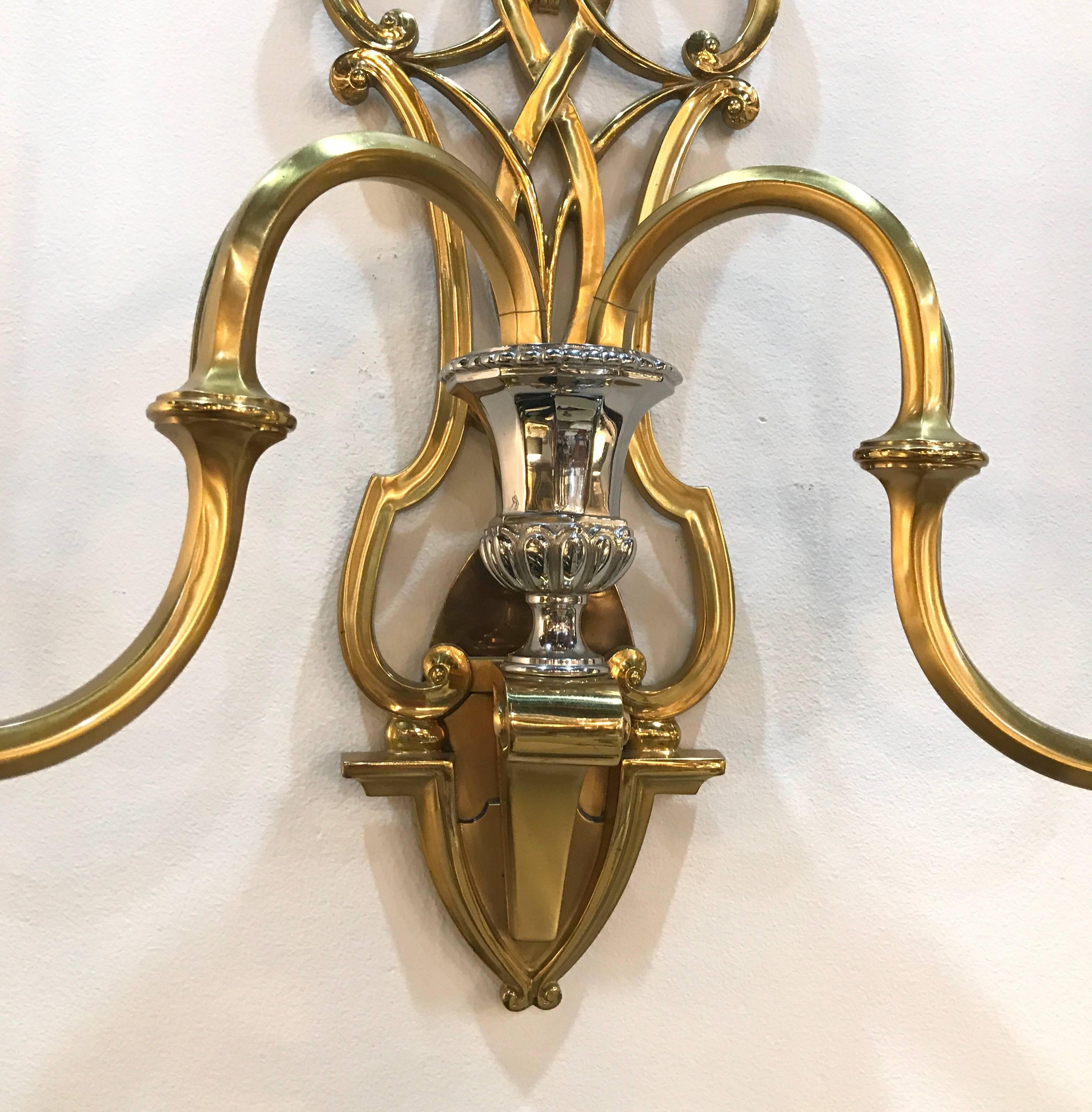 A graceful pair of polished brass French style sconces with nickel-plated accents. The plume tops with pretzel braid back shield with two electrified candles.