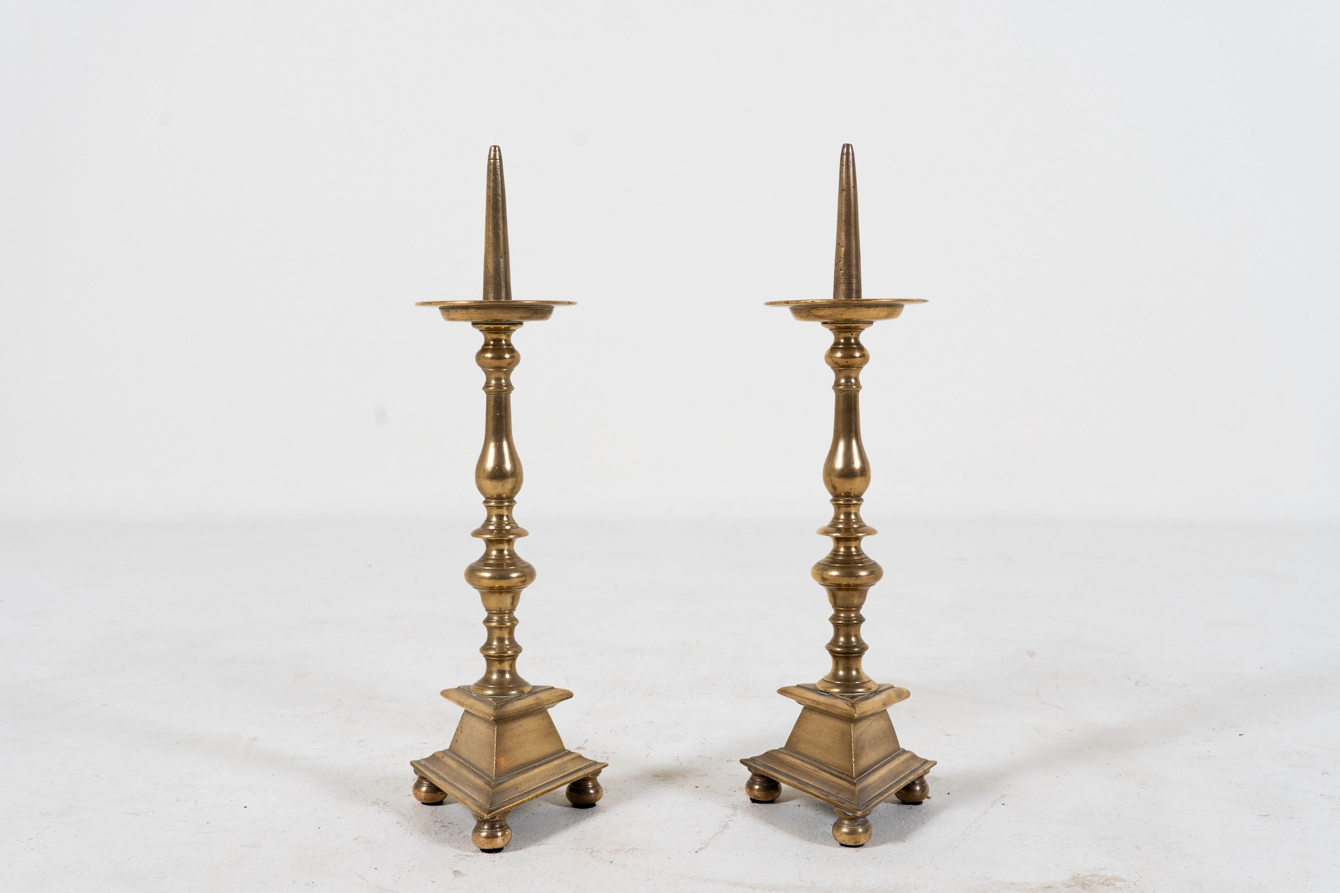 Diese großen und eleganten Kerzenhalter aus massivem Messing wurden in Avignon, Frankreich, gefunden und haben stilvolle dreieckige Sockel. Die ehemals polierte Oberfläche ist mit der Zeit und dem Gebrauch leicht abgestumpft. Der Kerzenbecher kann