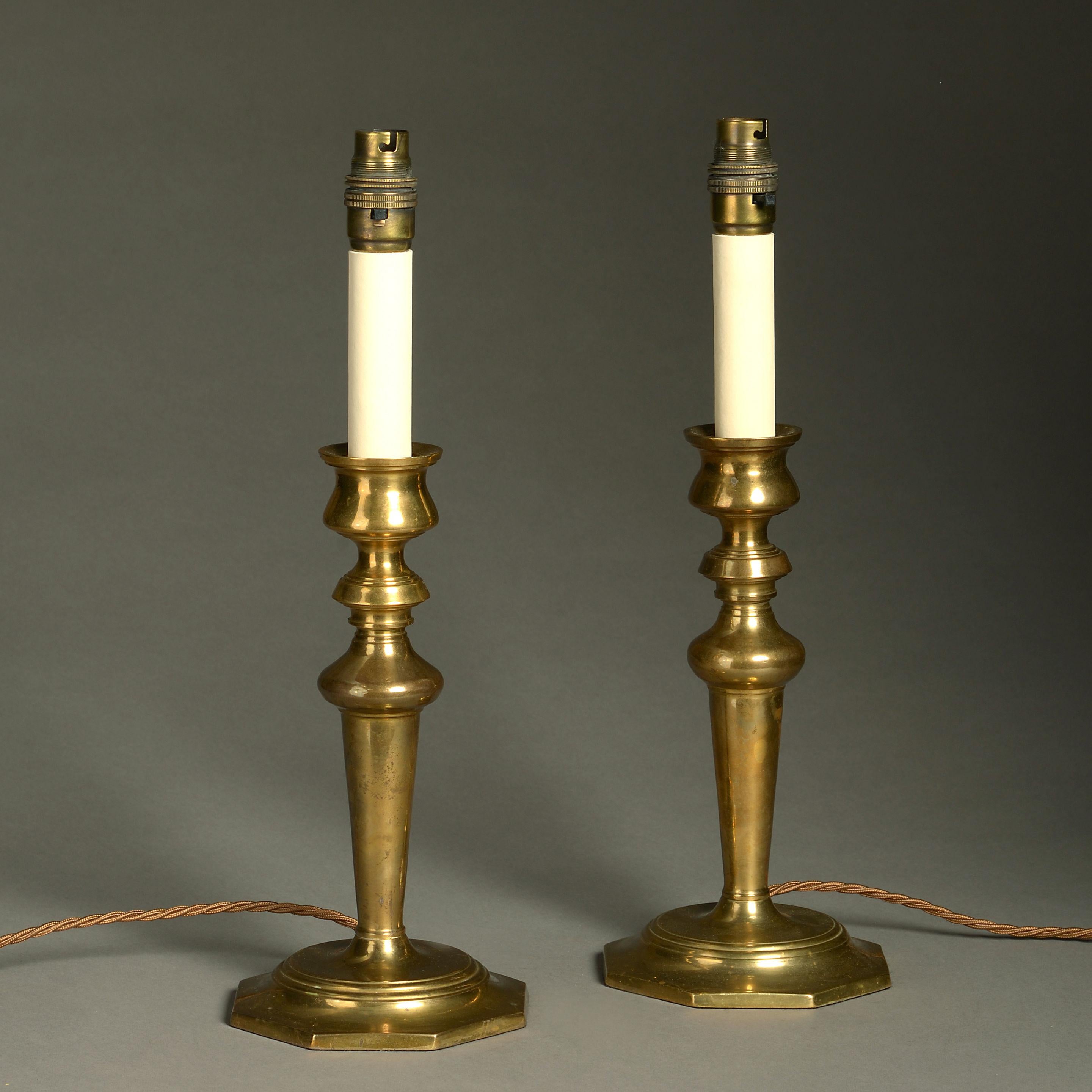 A pair of early 20th century brass candlestick lamps, having turned stems and octagonal bases. 

Dimensions refer to bases excluding electrical elements and faux candleholders.