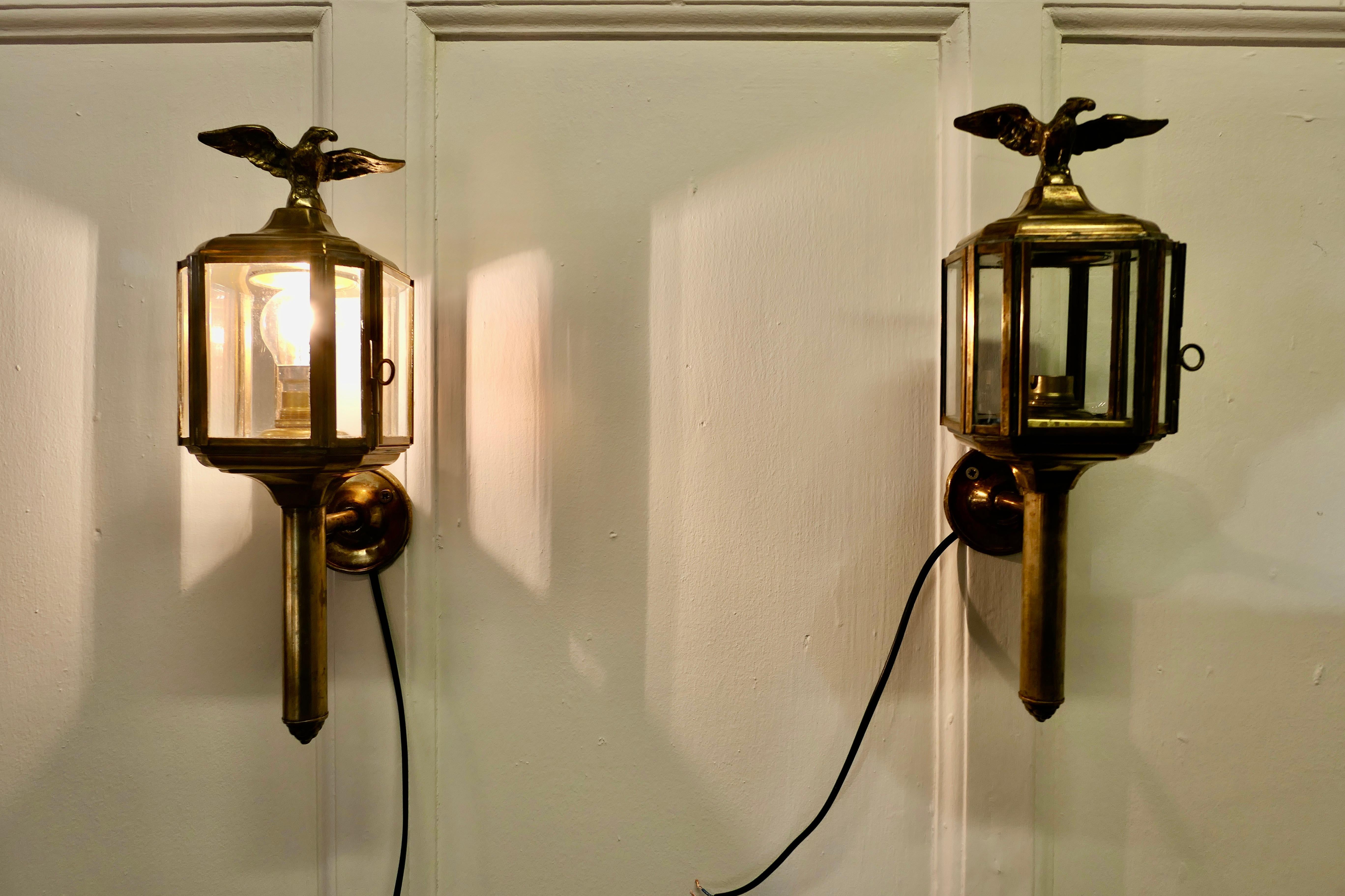 A pair of brass carriage style wall lights, lanterns with eagles.

2 Lovely pieces, they are wall lanterns made in brass 
These lights are in in good condition they have glass all of the way round, each giving a good illumination 
In good aged