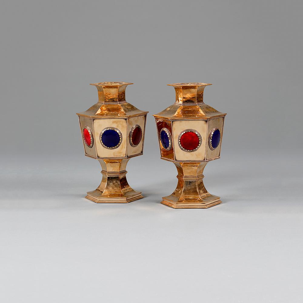 A pair of hexagonal brass flower holders, probably designed by Charles Robert Ashbee, the basins with red and blue enamel roundels.