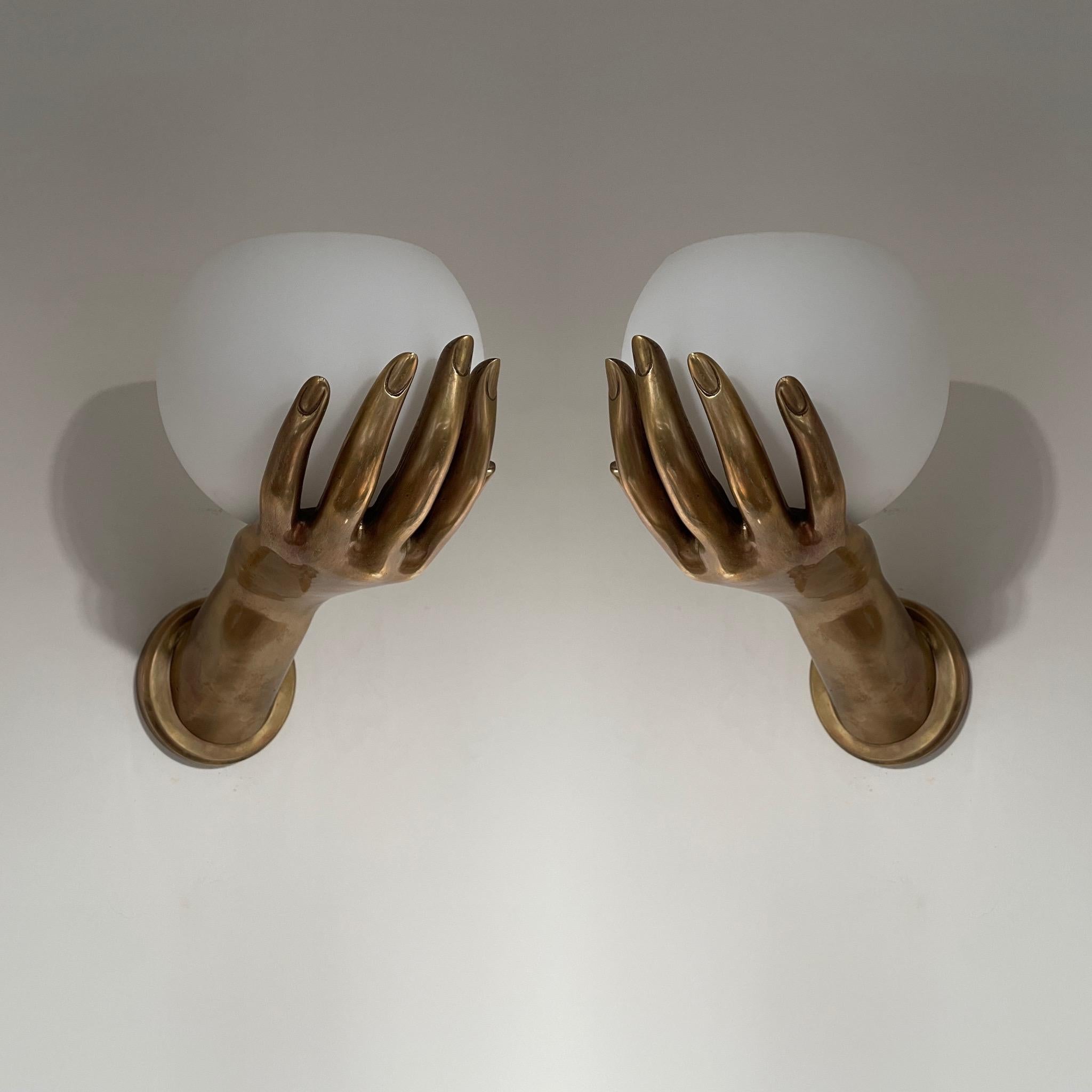 From our Studio Bucchi collection. A pair of wall lights in the form of hands holding frosted glass or opaque shades. Taken from a French mid century design, available in different finishes. Shown in antique brass. Very well cast and superb