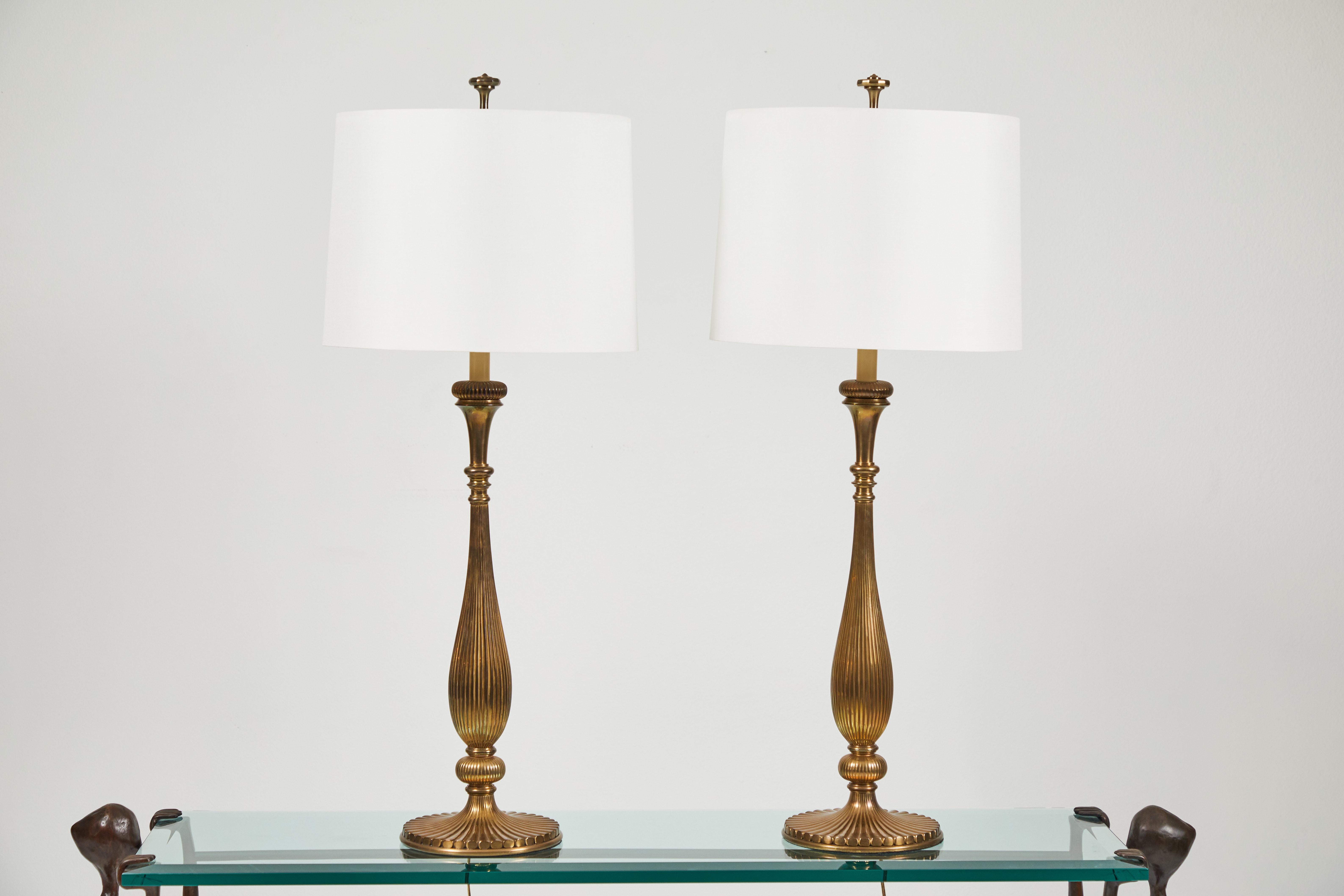 These solid Brass lamps by Chapman Lamps feature an elongated body with a ribbed detail. Lamps retain their original finials as well. New custom silk shades. Both lamps have the original felt and sticker on the bottom as seen in picture #5. These