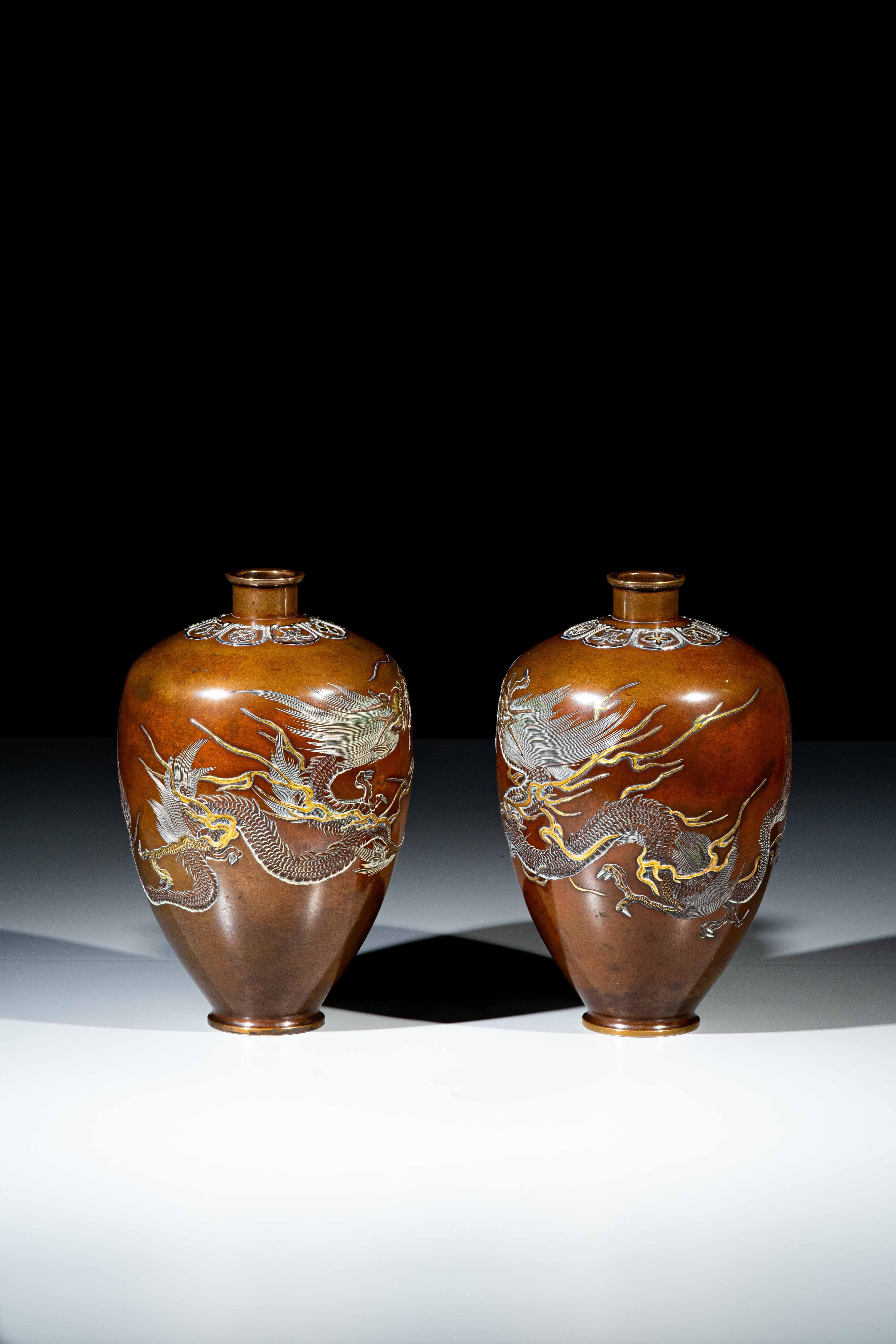 A pair of bronze vases with shishiaibori and iro-e takazogan inlays in relief in gold and silver and worked in kebori depicting two dragons, both embracing the vases with Nogawa company brands. The upper part has geometric decorations in relief in