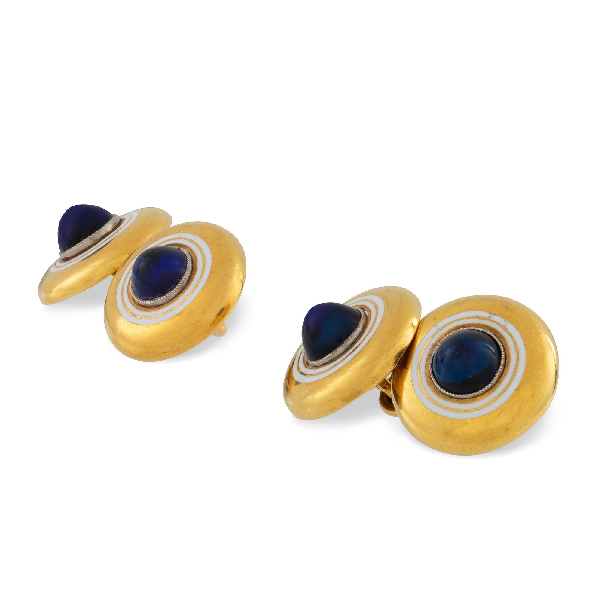 A pair of cabochon sapphire and enamel cufflinks, the centre a cabochon sapphire surrounded by two bands of white enamel on 18ct  yellow gold round discs with chain links, stamped 18ct, circa 1920, measuring approximately 1.5cm in diameter, gross