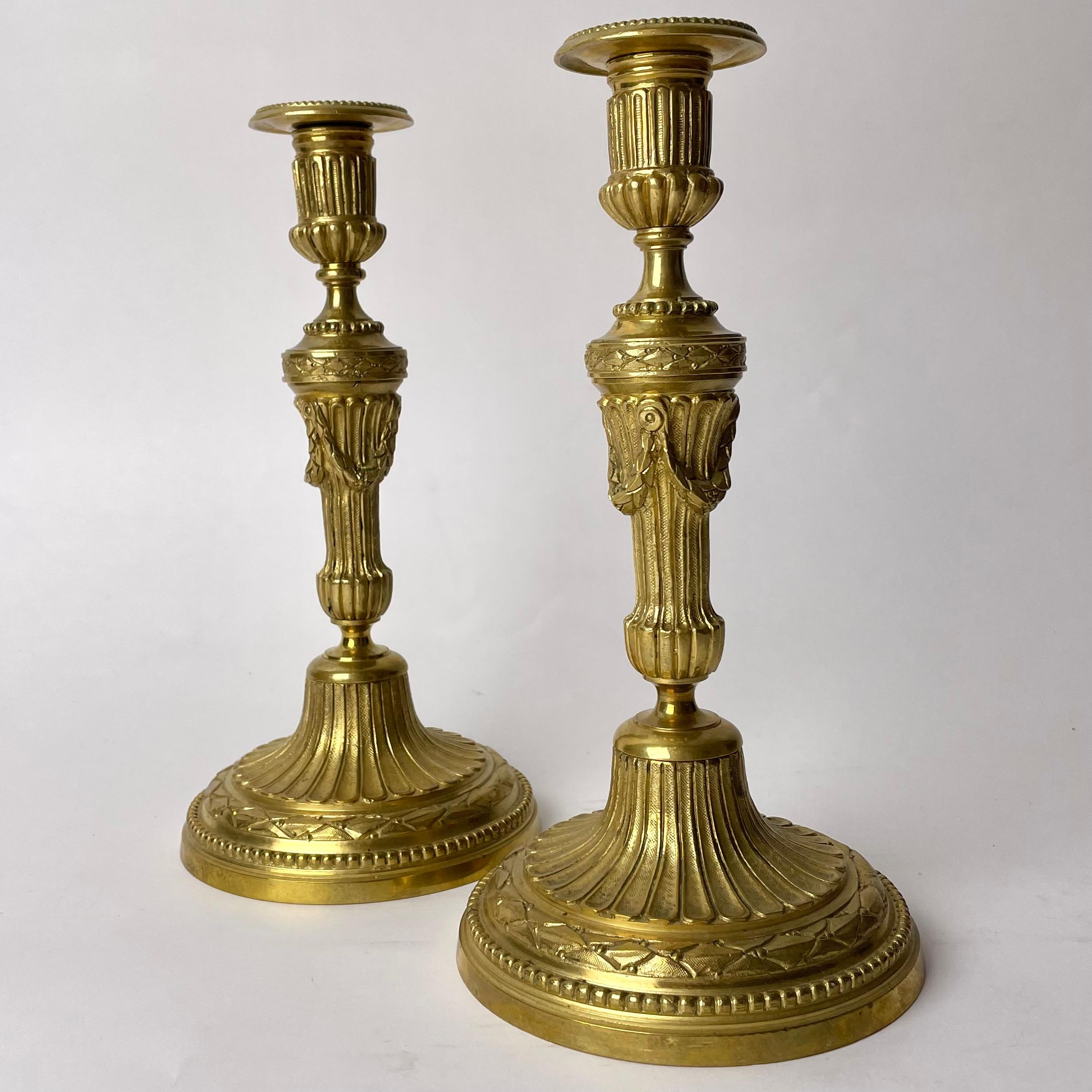 A Pair of Elegant and Ornate Gilt Bronze Candlesticks from the 19th Century. In the style of Louis XVI.

This pair of gilt bronze candlesticks are highly ornate in the style of Louis XVI, reflecting an appreciation for the elegant forms of classical
