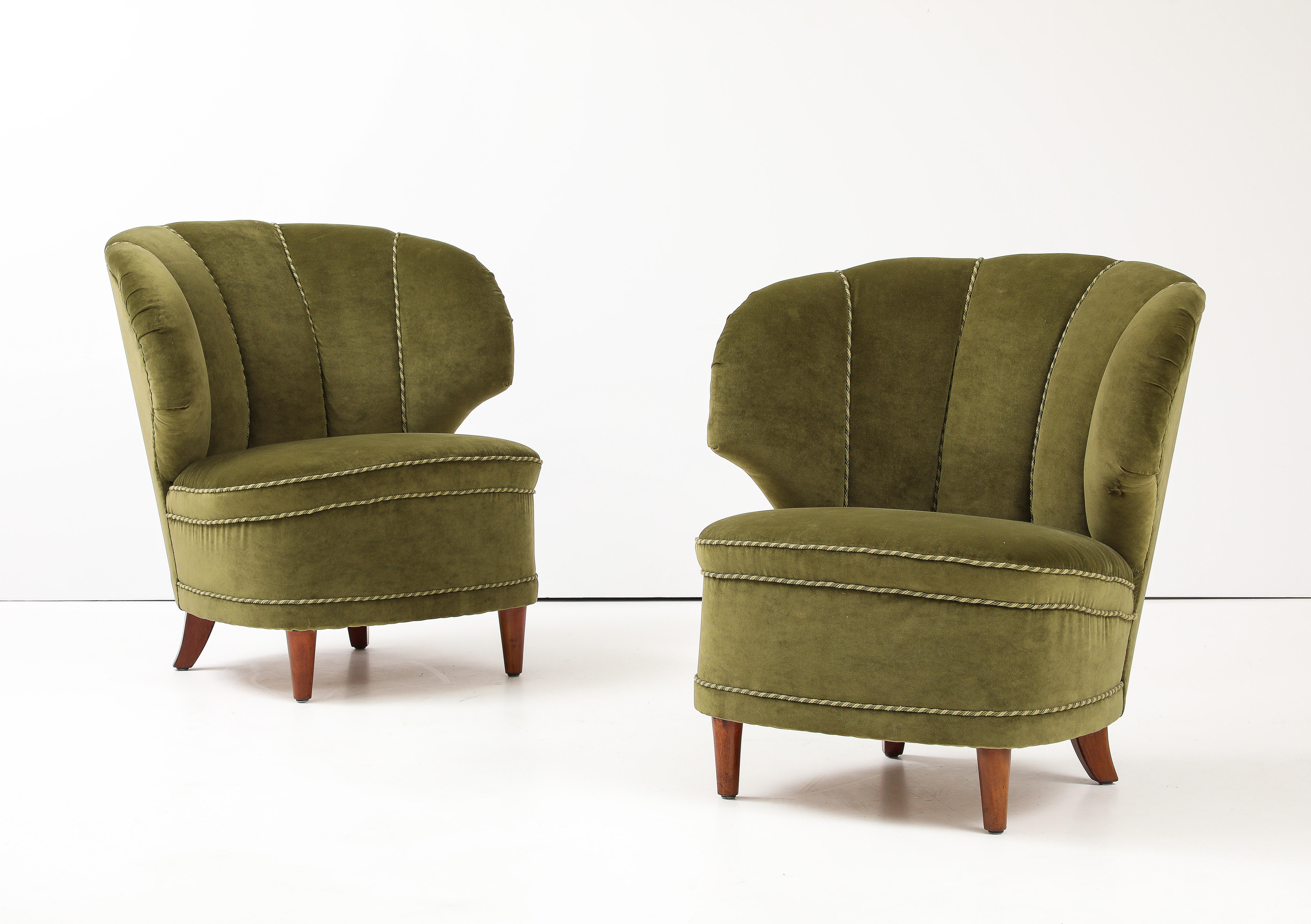 A pair of Carl-Johan Boman club chairs, Finland, Circa 1940-50, with curved and angular backrests, upholstered rounded seat raised on turned and tapered legs. Appears to be original green velvet upholstery in good condition with minor marks. The