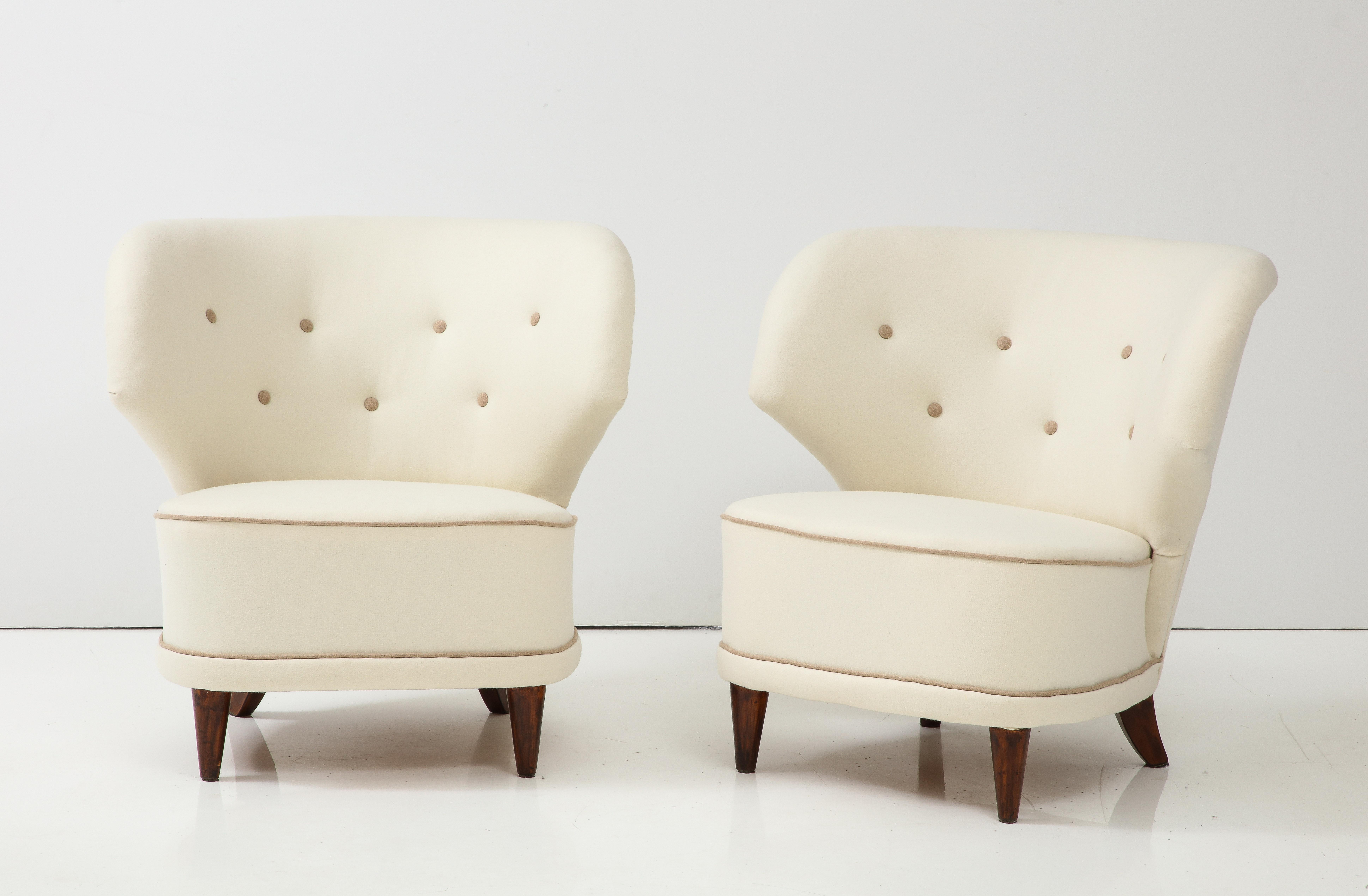 A pair of Carl-Johan Boman club chairs, Finland, Circa 1940s, with curved and angular backrests, upholstered rounded seat raised on turned and tapered legs. New off-white wool upholstery. Produced by Oy Boman Ab