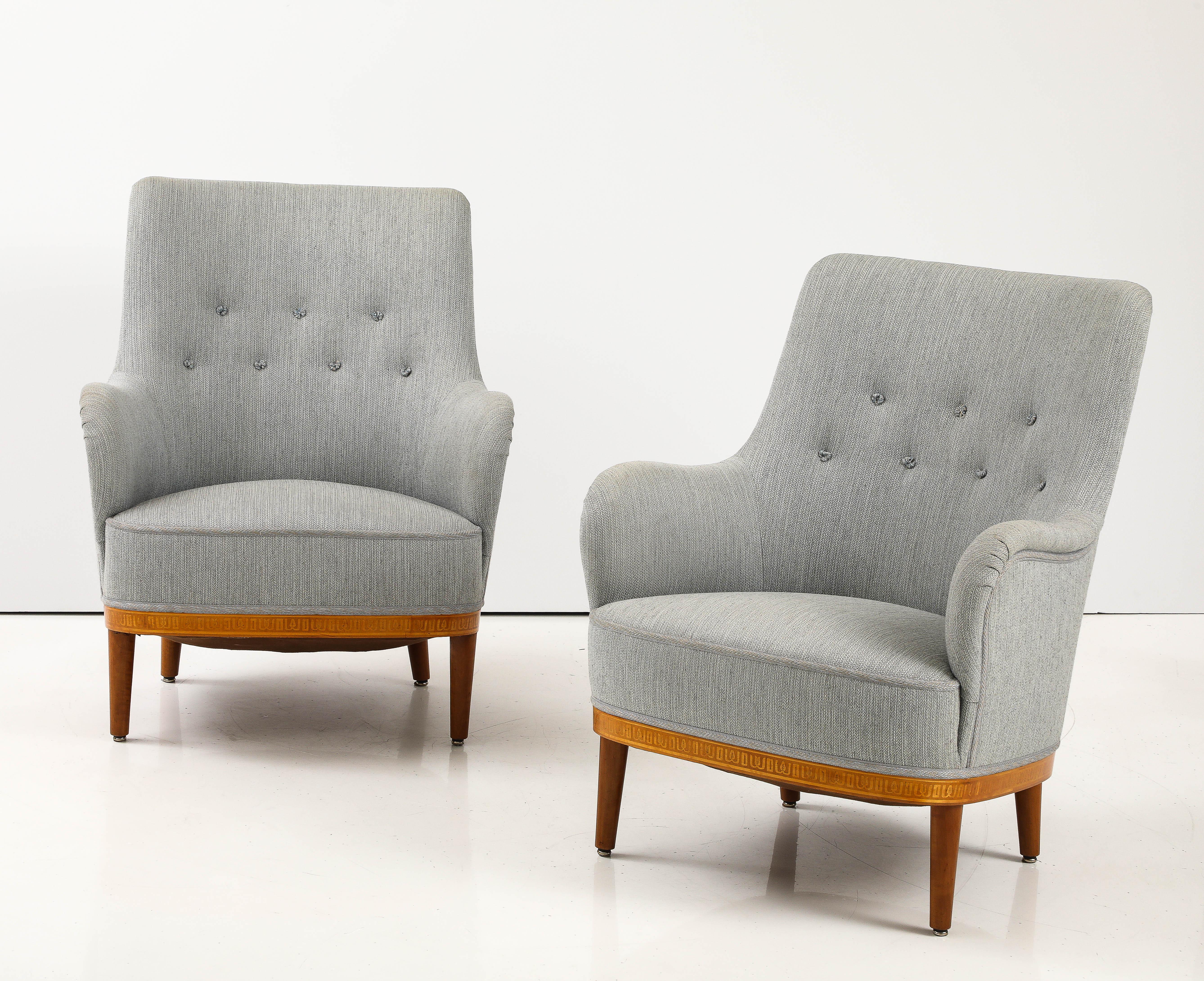 A pair of Swedish Carl Malmsten birch and mahogany armchairs, Circa 1940s, with curved upholstered seat and back, a neoclassical inspired fruitwood inlaid frieze raised on circular turned and tapered legs. The underside with an upholsterers label.