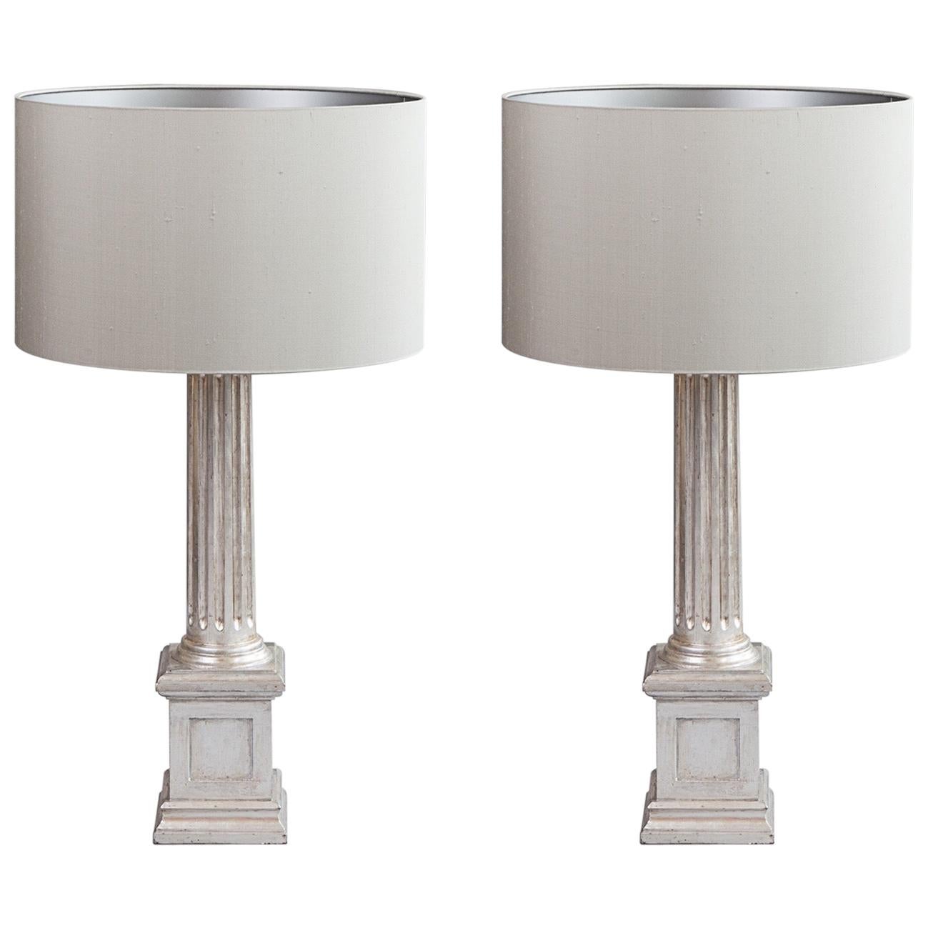 Una coppia di lampade da tavolo a colonna in legno intagliato e dipinto in argento dorato