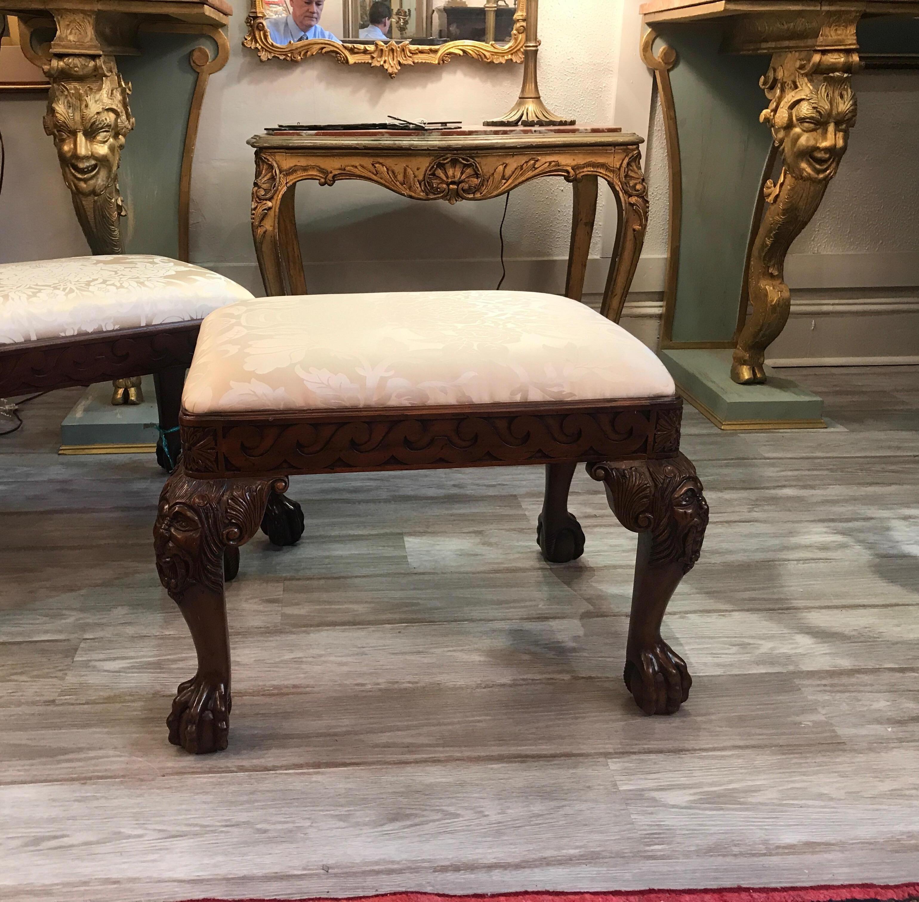 A pair of carved mahogany benches with damask fabric. The heavily carved legs with mask figure on the knees, the feet with ball and claw.
  