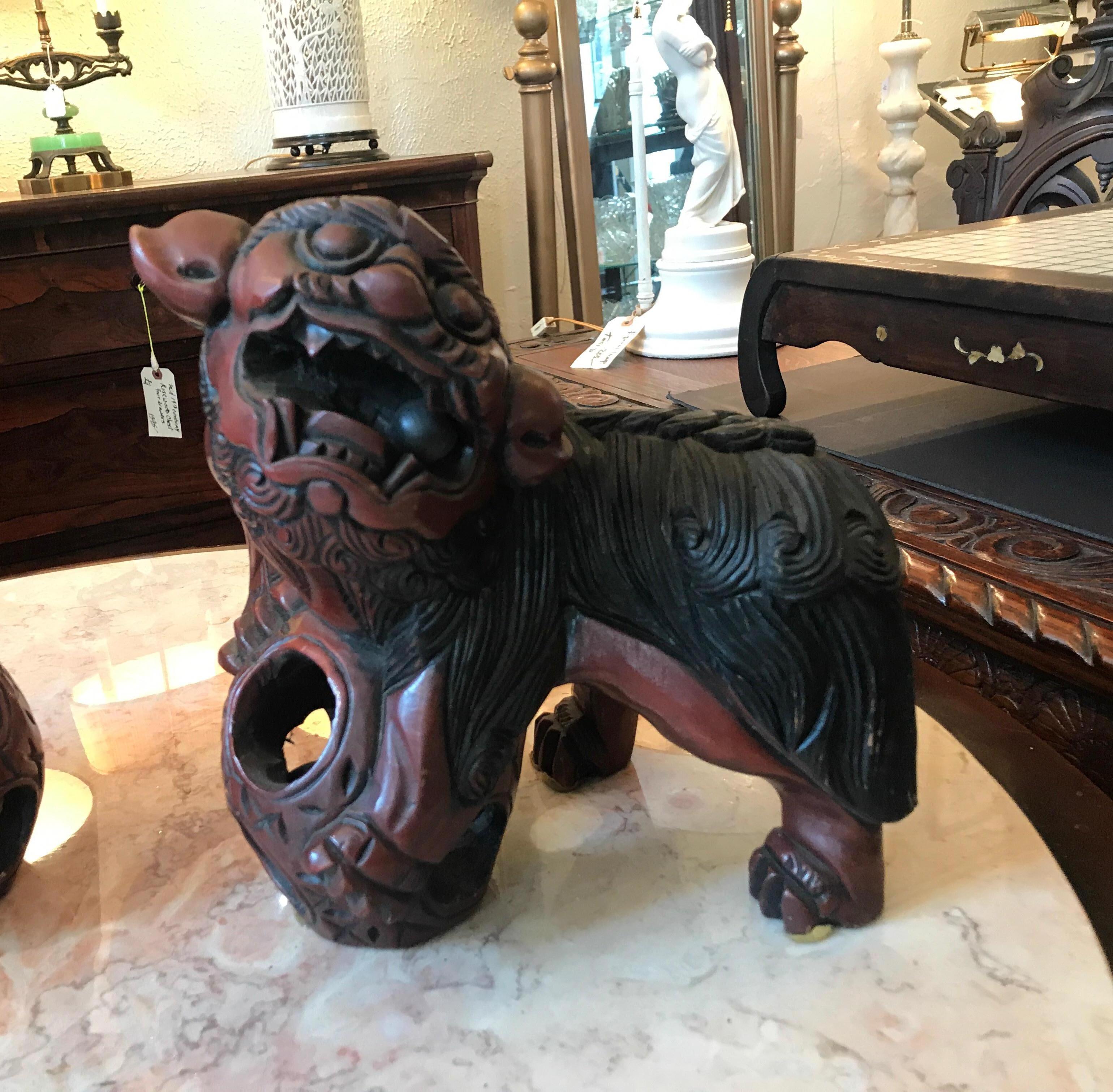 A pair of carved wood and cinnabar lacquer food dogs. The dogs, each carved with a ball in each in the mouth of the dogs and in the circular base of the front foot. Original pair that are a mirror image of each.