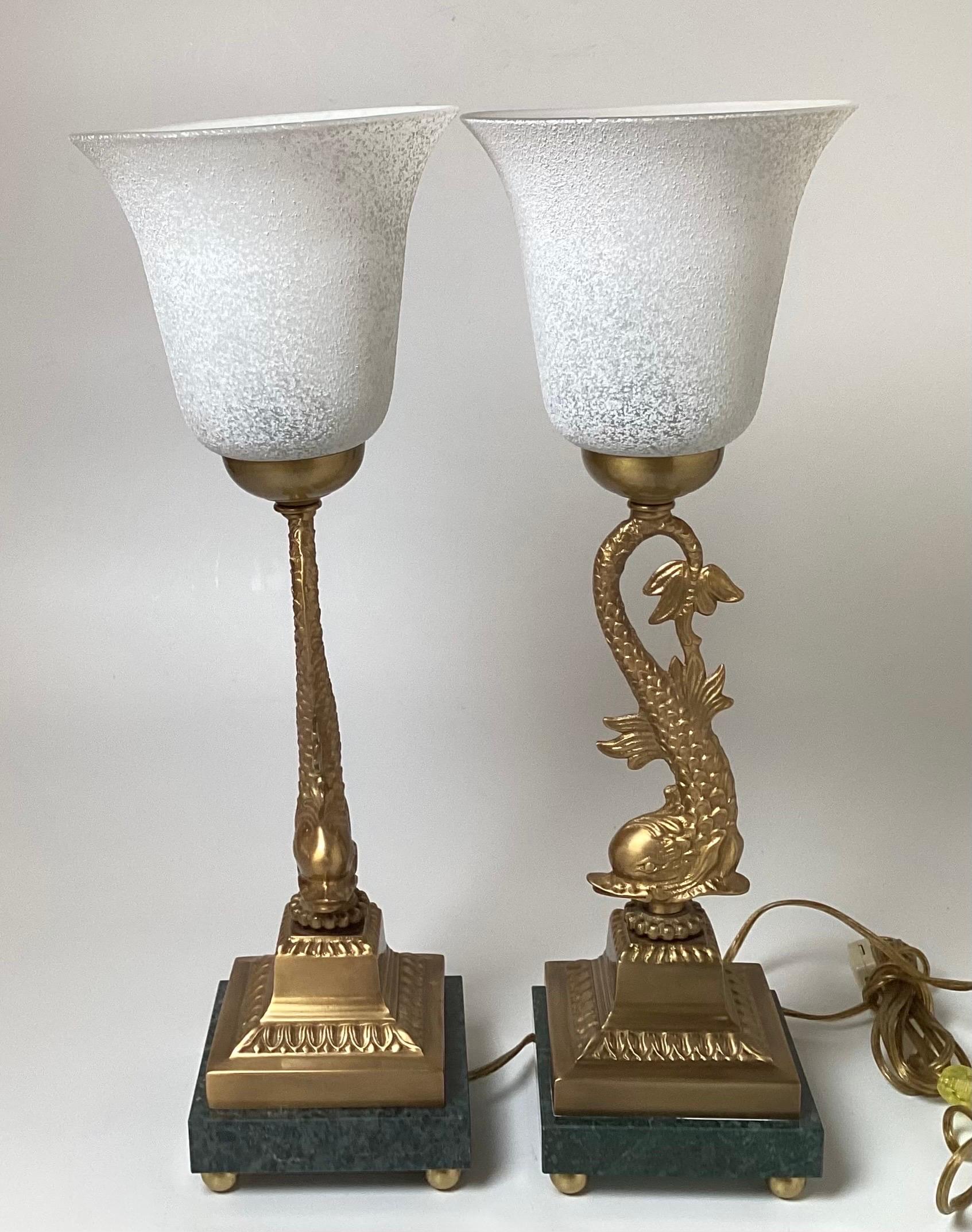 A Pair of cast brass and marble dolphin motif buffet laps with frosted white glass shades. The lamps are 19 inches tall tot he top of the shades and 6.5 inches in diameter at the top, with a 5.5 inch square base. The on-off switch is on the cord.