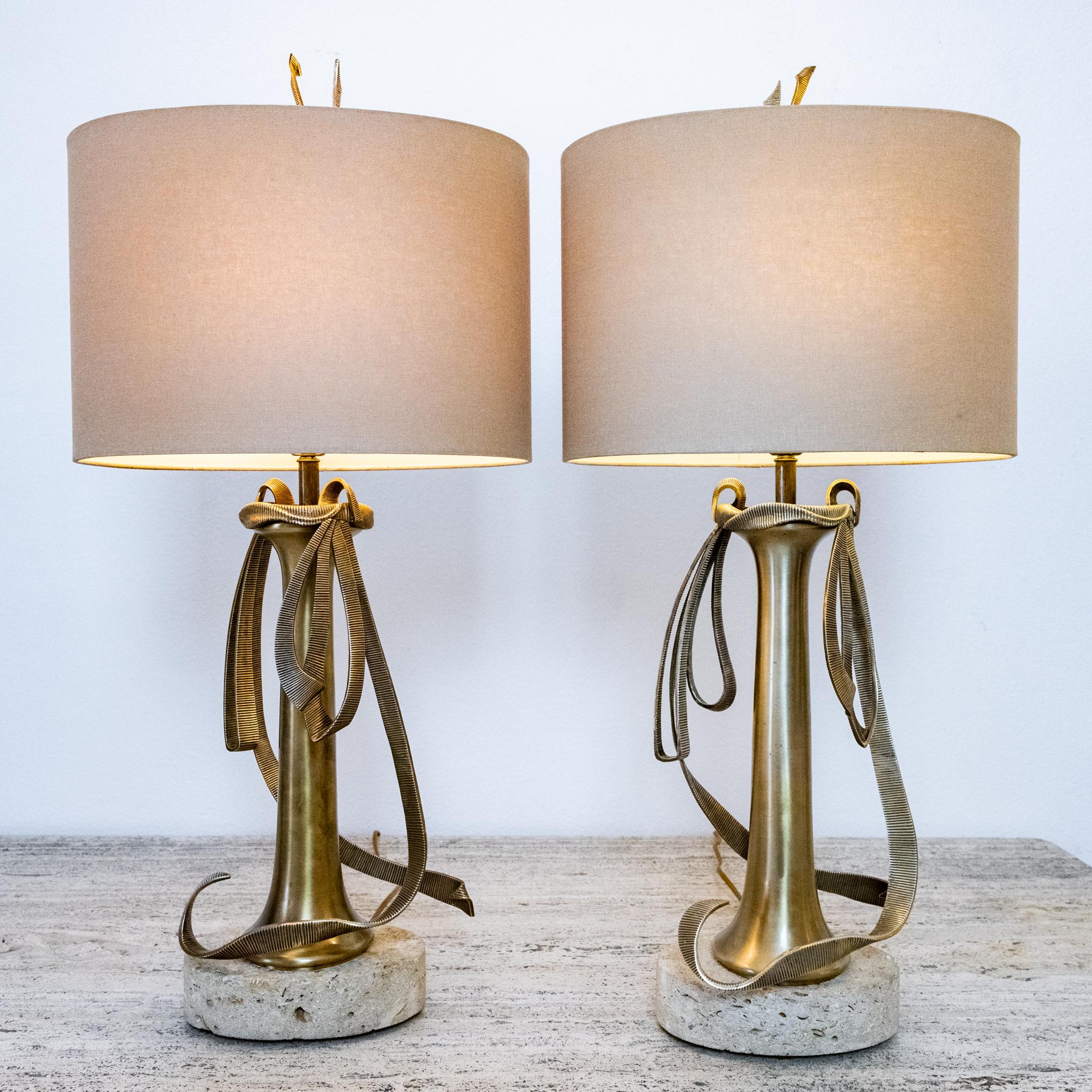This pair of Chapman lamps, dated 1999, feature a beautiful brass stem and brass ribbon detail. The travertine base adds to the interest of these lamps by bringing in an additional material. Perfect for bedside or living room lamps, these