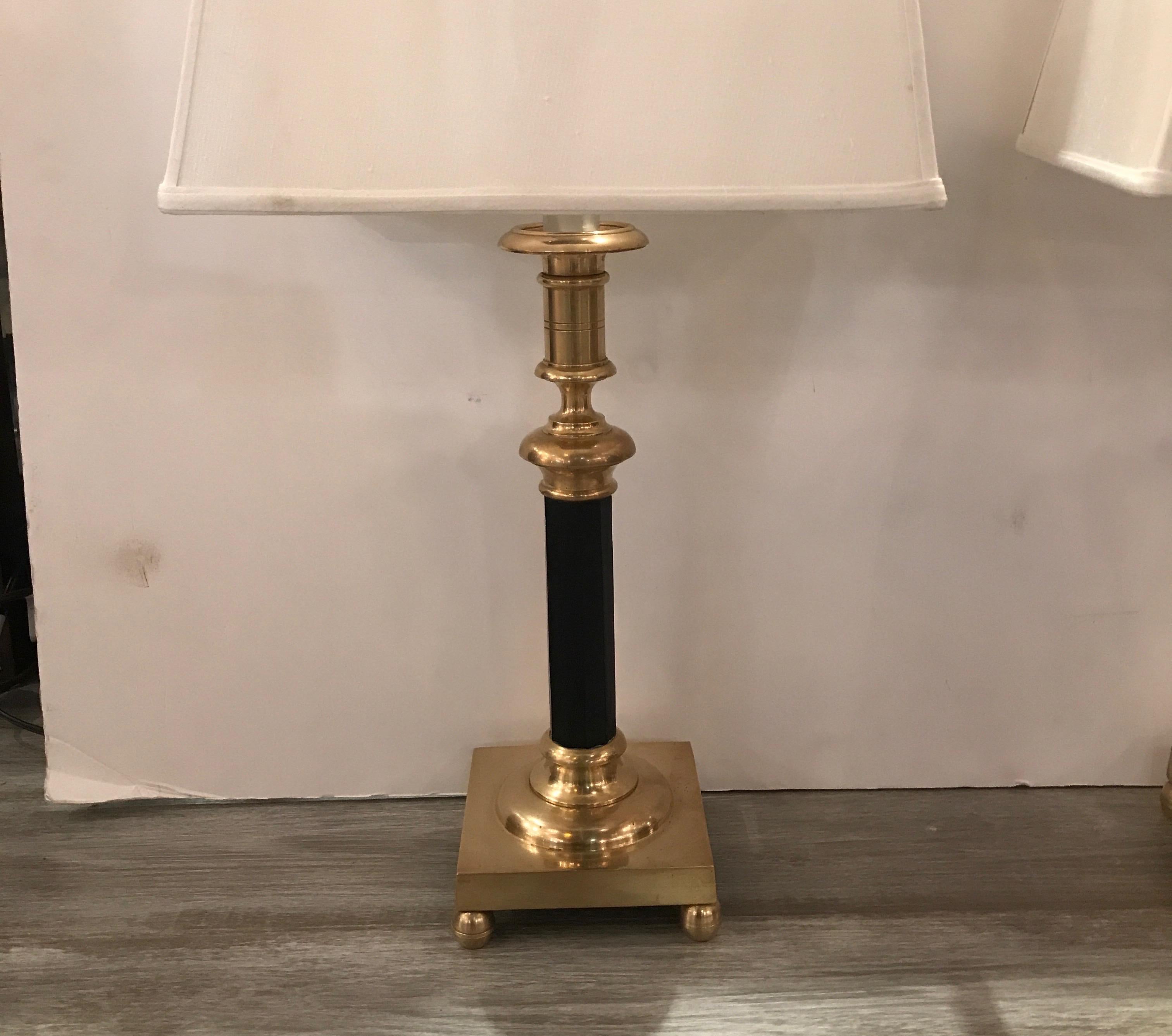 Elegant pair of solid polished brass candlestick lamps by Chapman The heavy candlestick for with black enamel column center with tall harp form finial. The lamps take 2 bulbs for extra light. The shades are for photographic purposes only and not