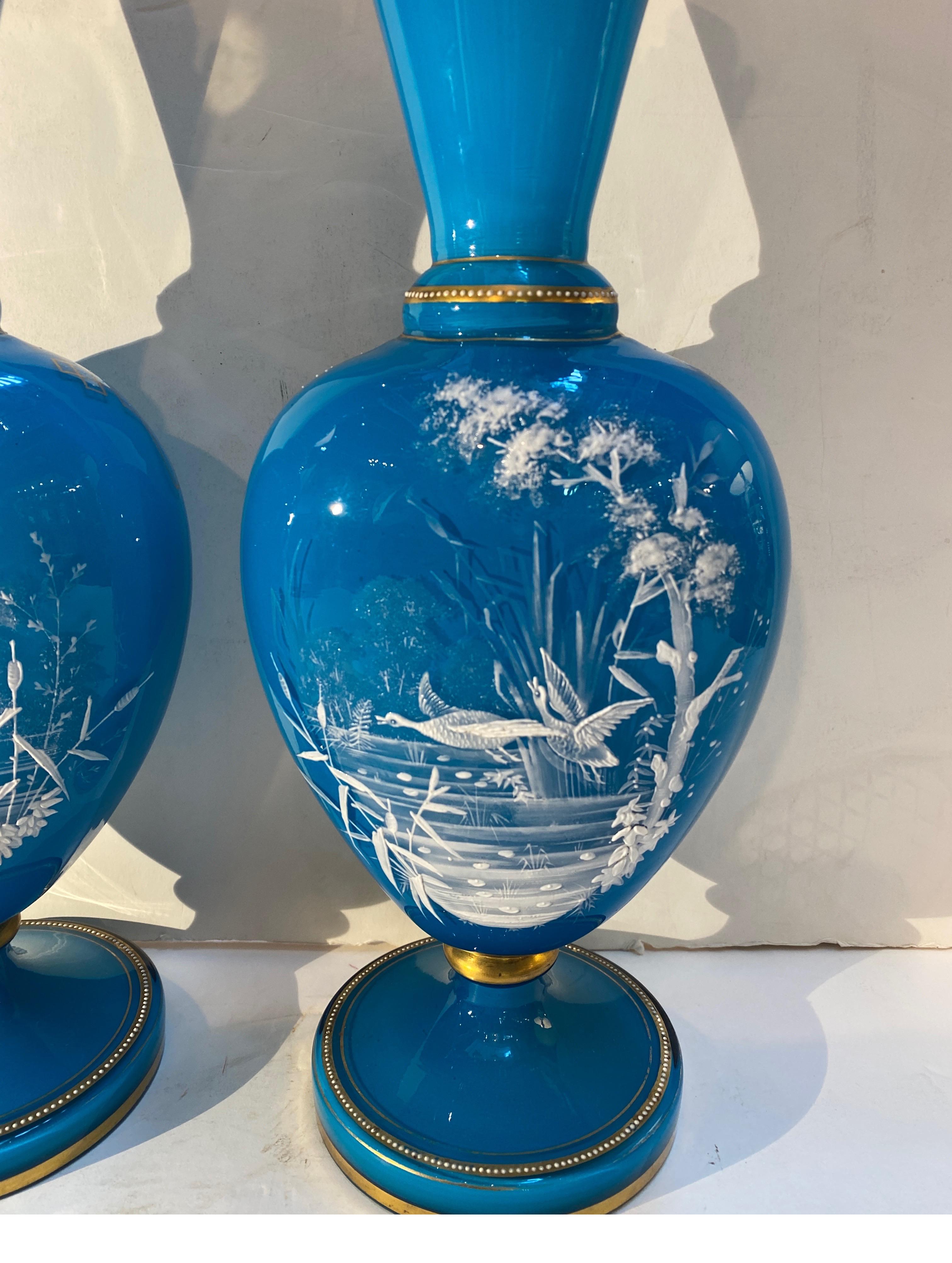 A pair of vibrant Celest blue opaline manel vases with hand gilt decoration.  The fronts with delicate pate sur pate style enamel water scenes.  The tops with cut decorative edging with gilt highlights.  The interior is white opaline glass with an