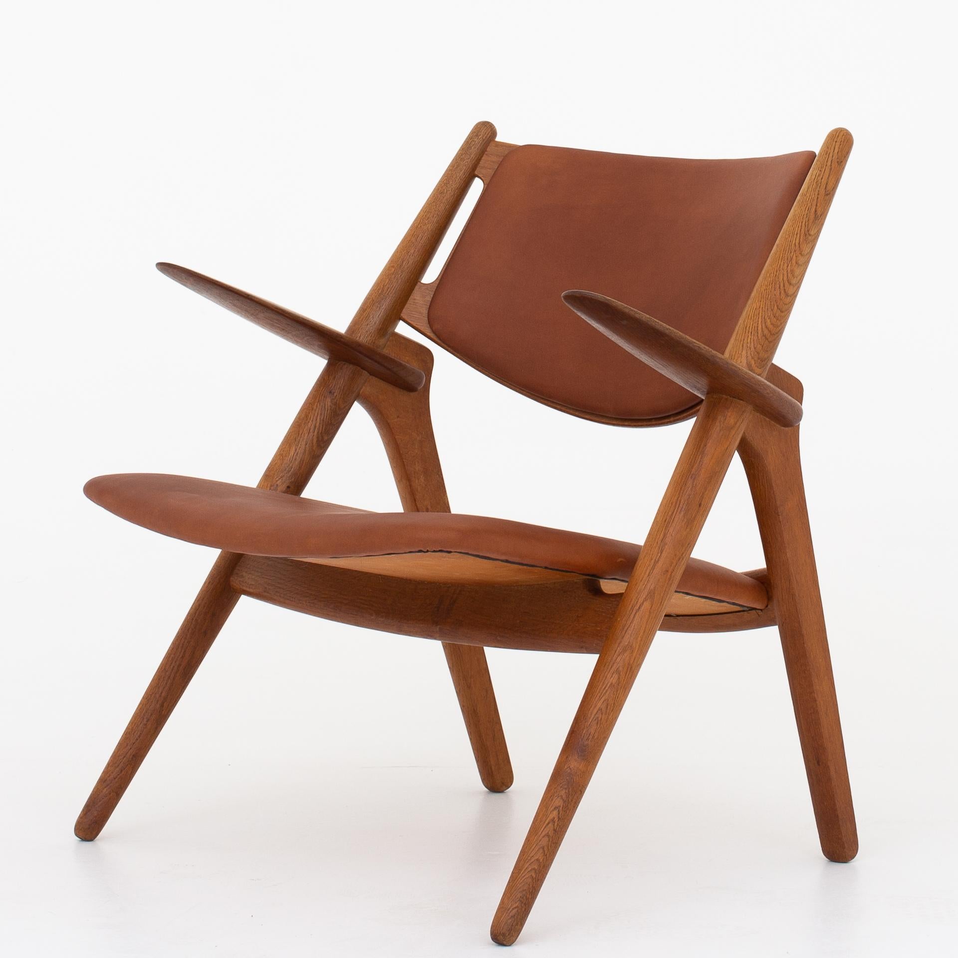 Two CH 28 - 'Sawbuck' easy chairs in patinated oak, reupholstered in Dunes Cognac leather. The leather has been treated with leather grease. Maker Carl Hansen.