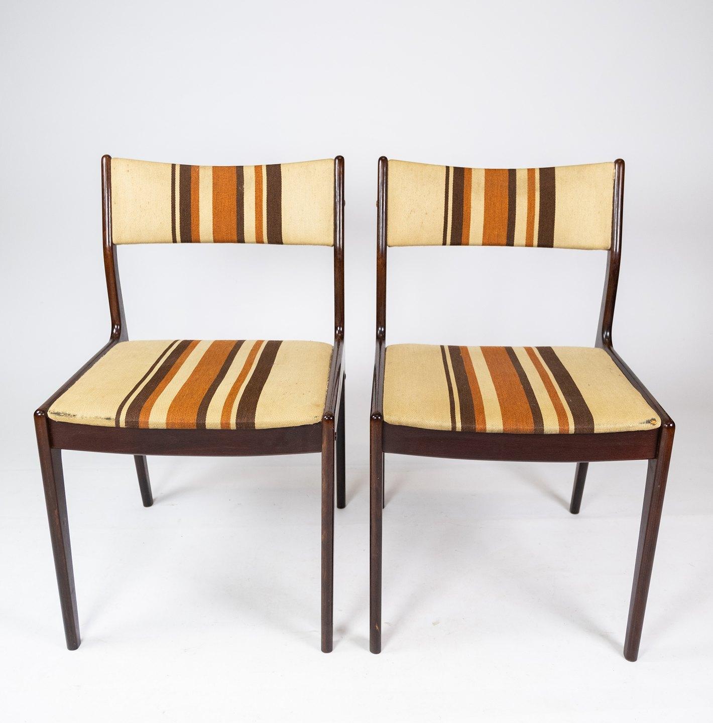 Cette paire de chaises, provenant de l'usine réputée Uldum Furniture au Danemark, incarne l'éthique emblématique du design danois des années 1960. Fabriquées en bois foncé et revêtues d'un tissu rayé clair, ces chaises présentent un mélange