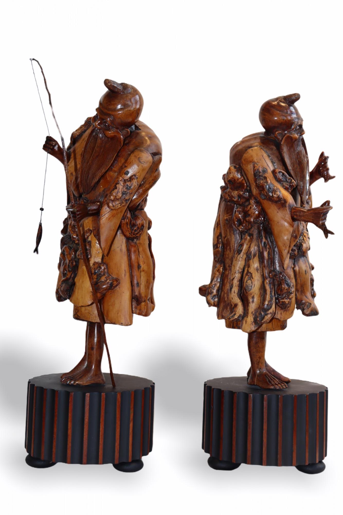 This pair has been meticulously carved into root wood, 18th-19th century. The natural form of the wood carved as emerging spirit of the monks who have been fruitful in their fishing endeavor. Both of them are showing their catch. The root wood has