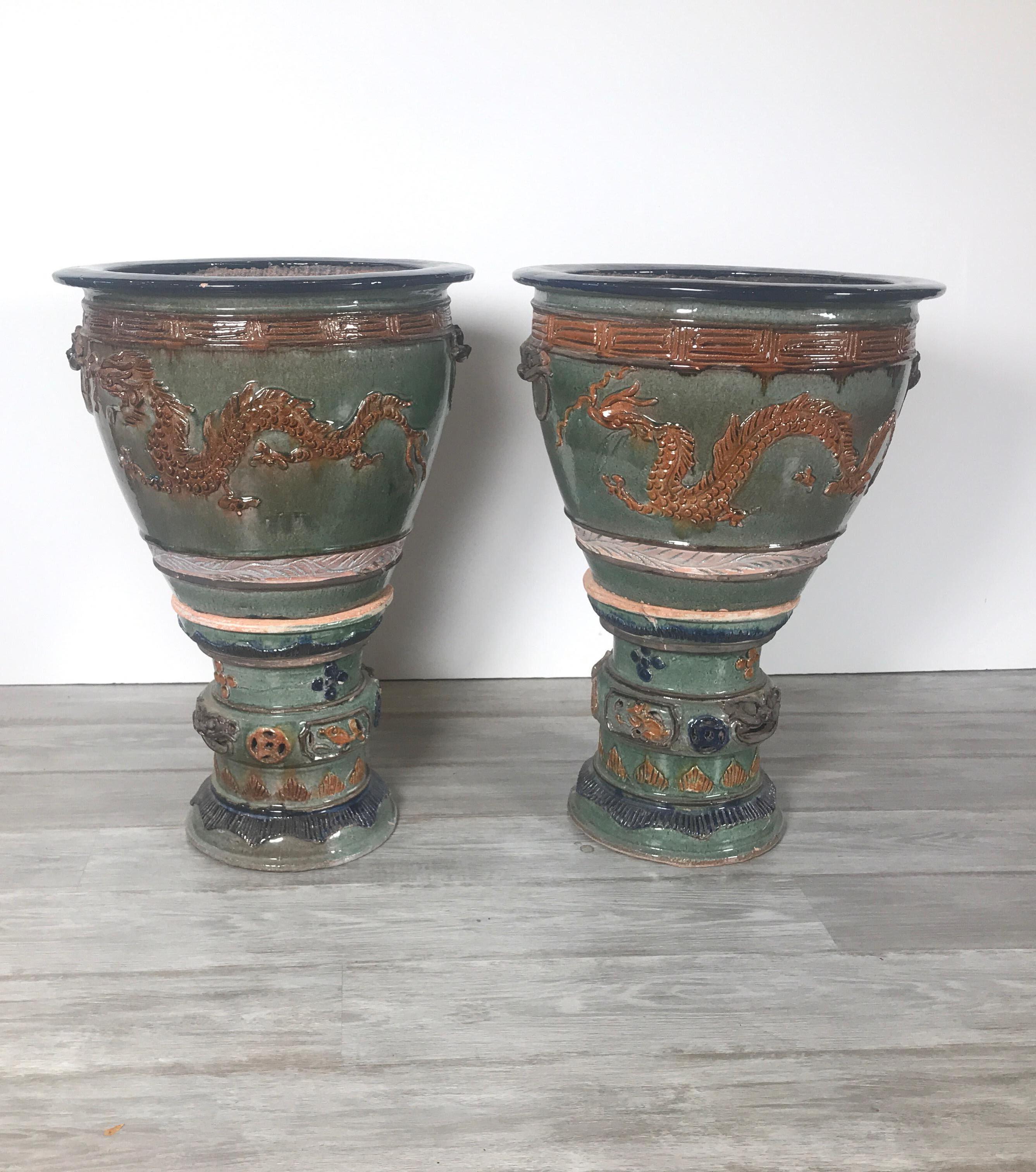 A vibrantly colored pair of planters with separate pedestal bases, Chinese, mid-20th century the terracotta with a bright glaze of sage green, cobalt blue, orange and brown in a dragon motif. Some expected minor chips on the edge. The pots with