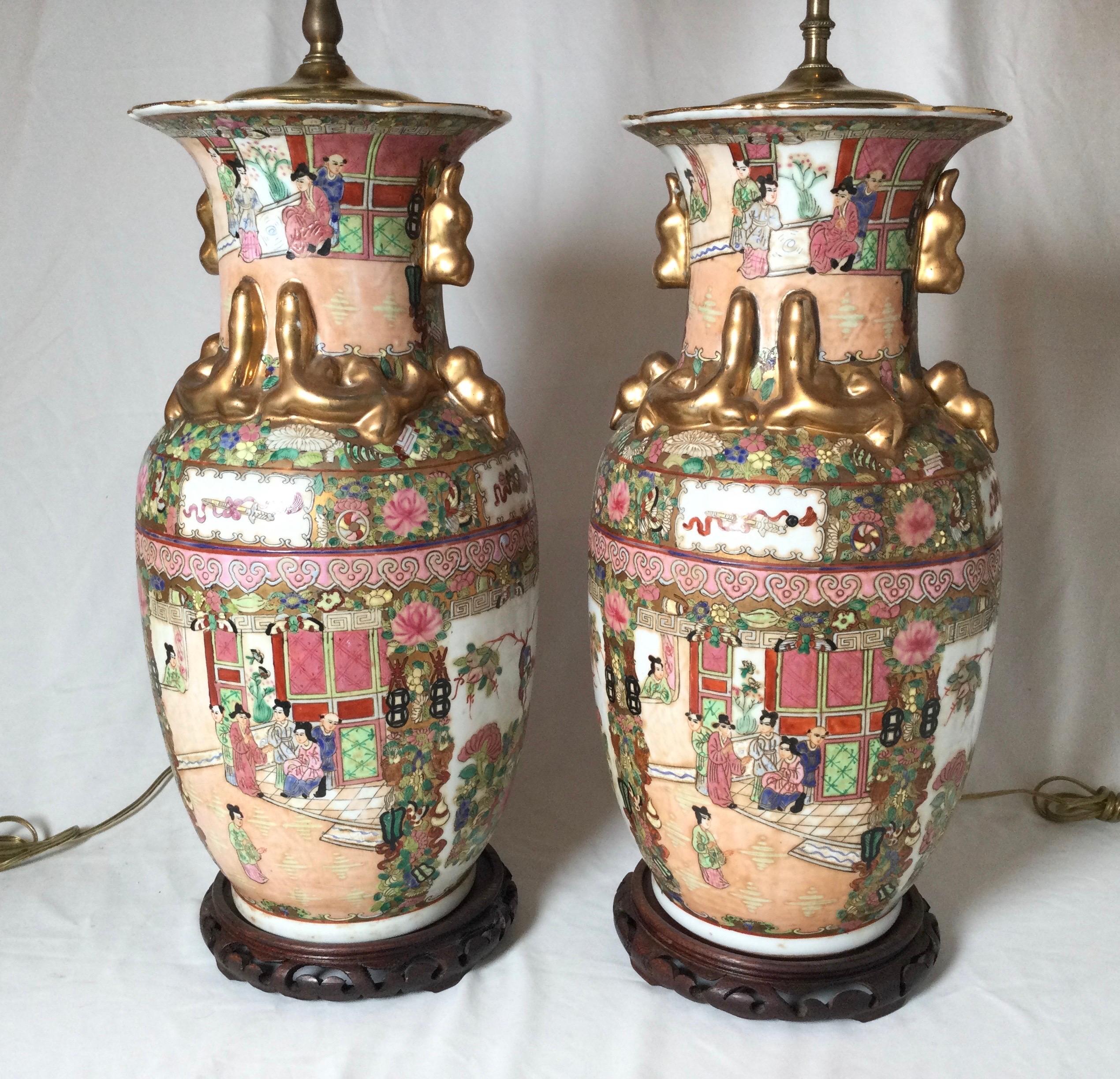 A pair of mid 20th century Chinese porcelain lamps, with wood Asian style bases. The hand painted porcelain in a Chinese Export Style with gilt dragon handles. 36 inches with a shade, 25.5 inches to the top of the socket, 9 in diameter.
