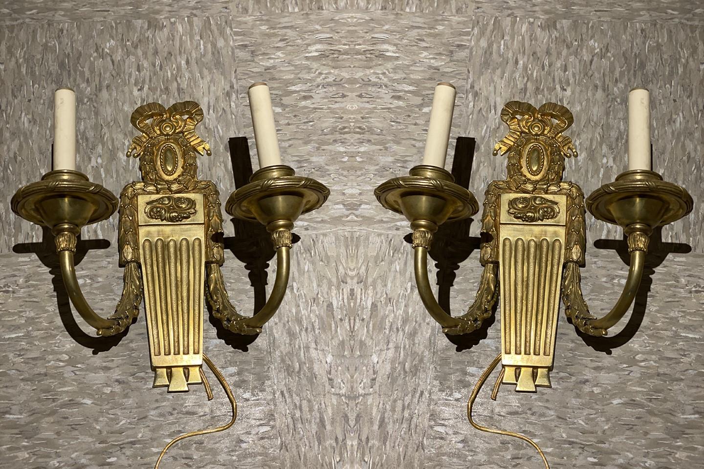 Un par de apliques neoclásicos de bronce dorado Caldwell de hacia 1920 con dos luces