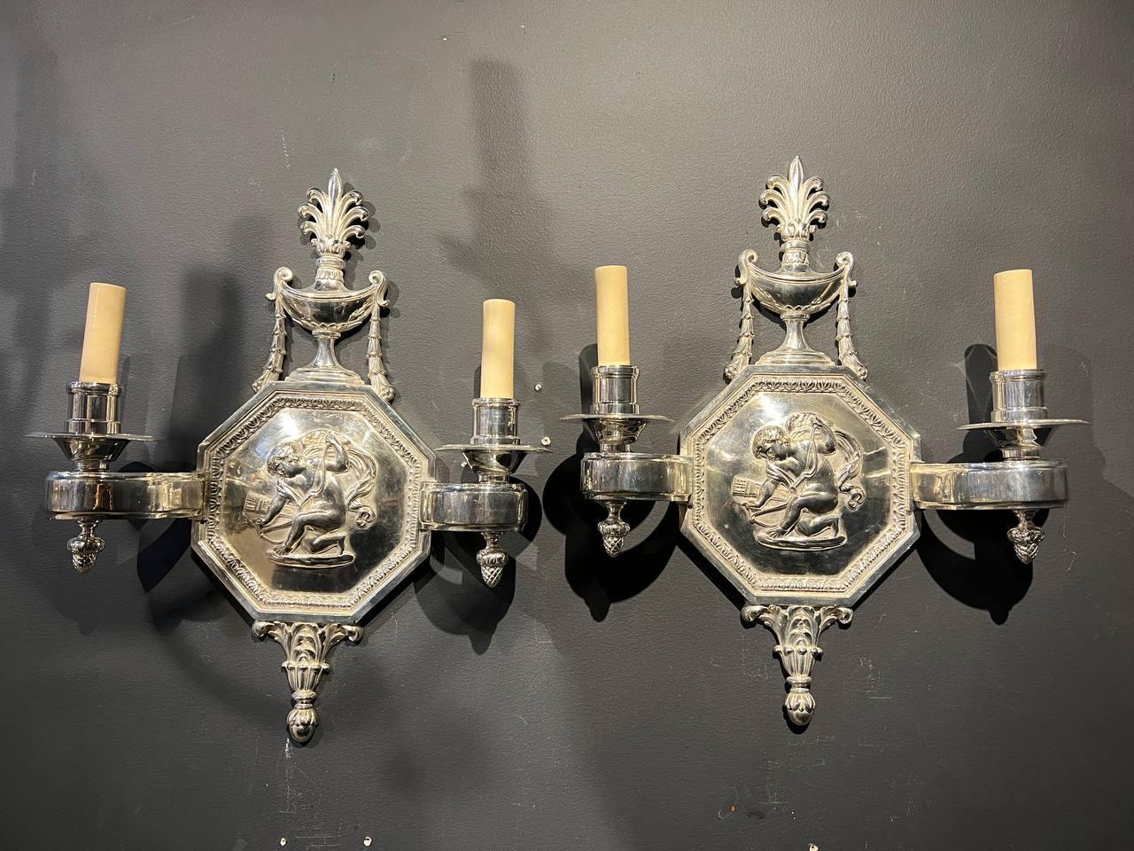 A pair of circa 1920's Caldwell silver plated sconces with cherubs and unusual scrolled arms
