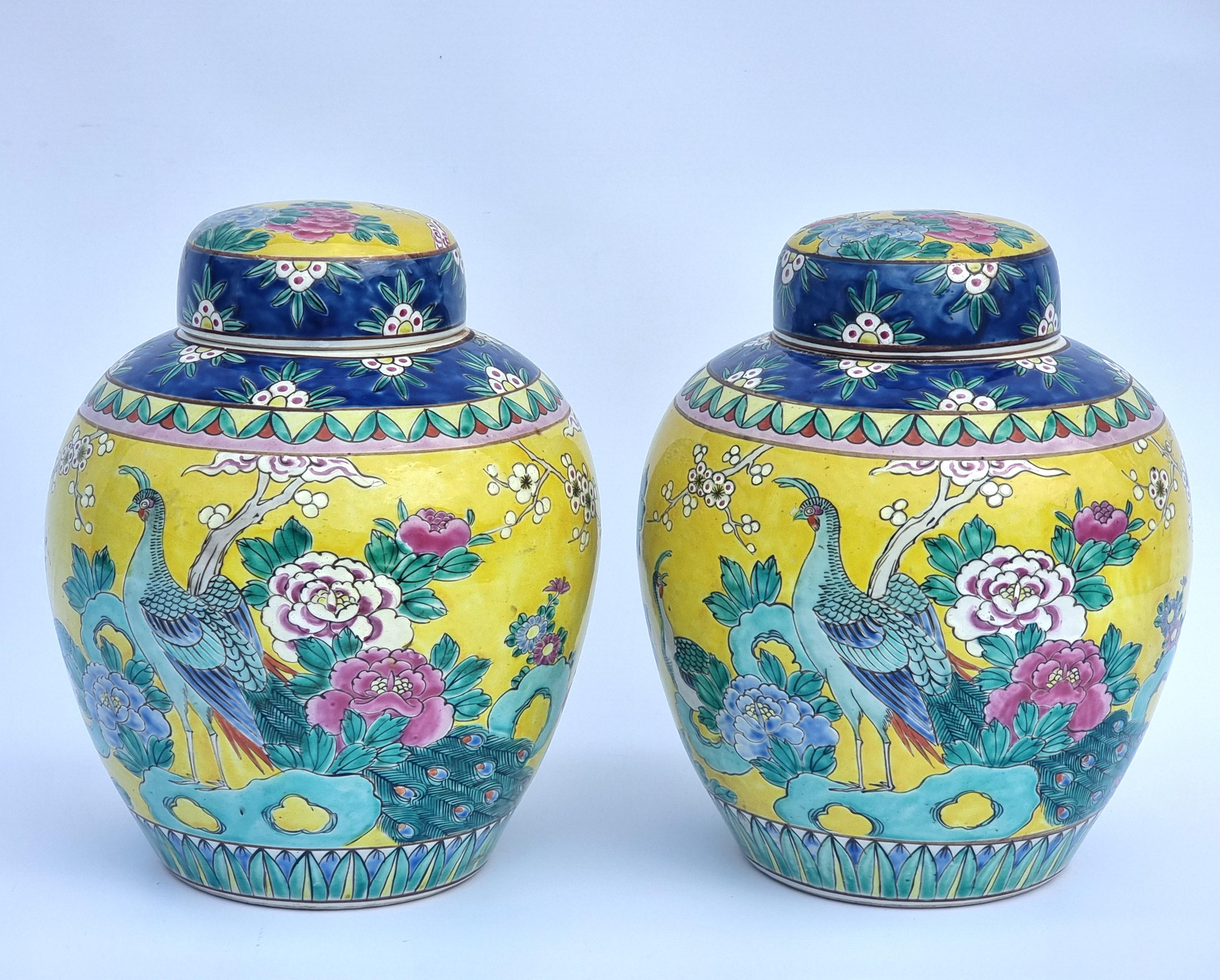 Cette paire de pots à gingembre et de couvercles en porcelaine chinoise, très décoratifs, présente un magnifique fond jaune et bleu vif, peint à la main dans une variété d'émaux riches en couleurs. Le décor comprend des oiseaux exotiques parmi des