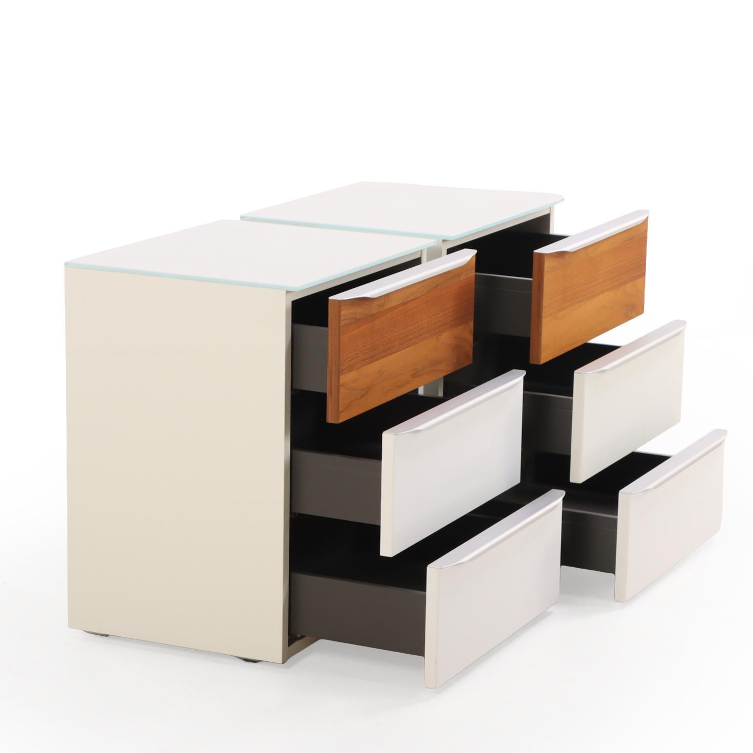 Paire de tables de nuit en laque épurée de Hülsta, Allemagne. Chacune comprend trois tiroirs, un plateau en verre, une garniture en aluminium brossé et une touche de bois chaud. Leur forme épurée et le mélange équilibré des matériaux soulignent la