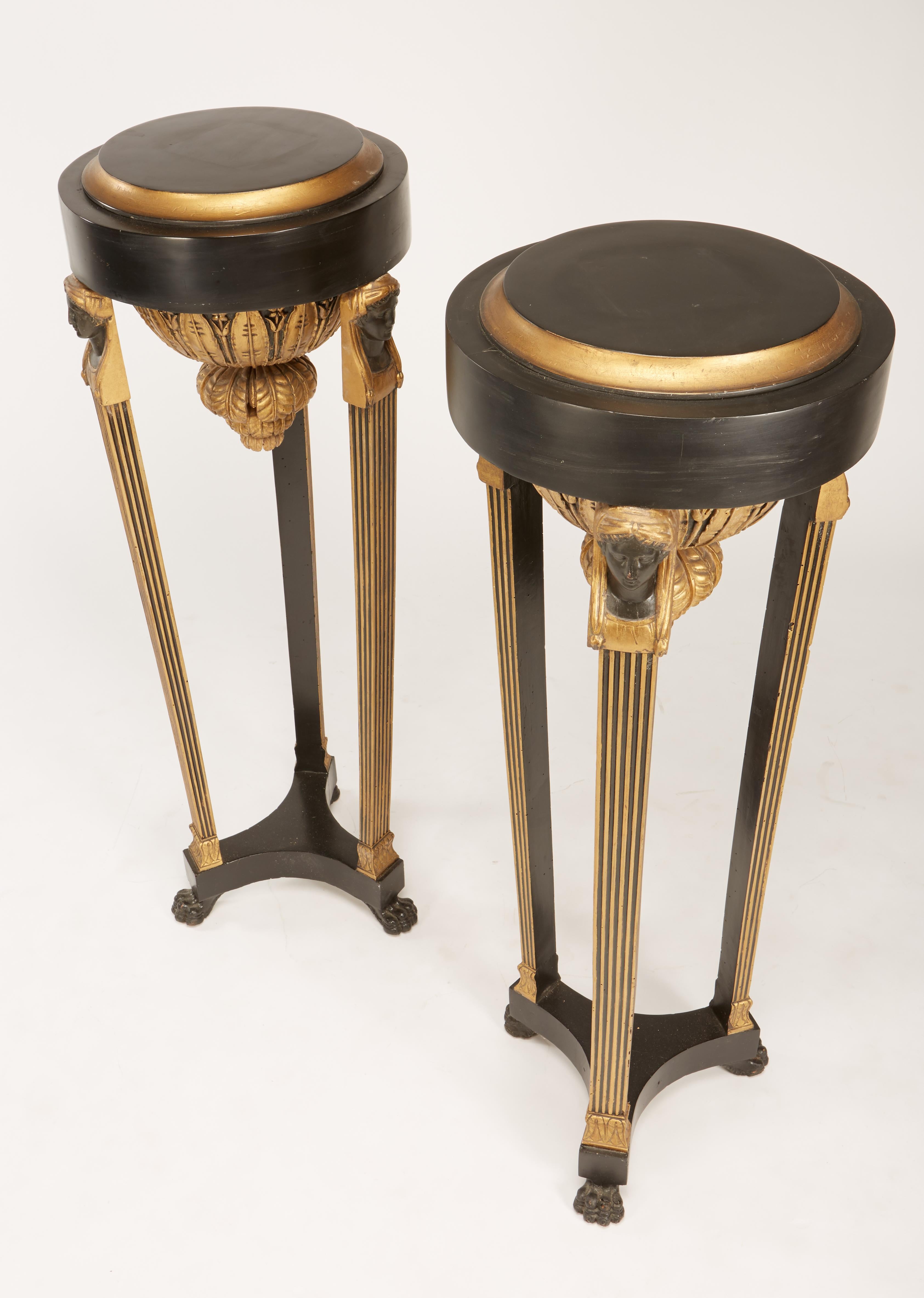 A fine matching pair of Continental Italian neoclassic black painted and parcel-gilt torcheres having urns with female bust on top of fluted legs on paw feet. Later tops, top diameter is 13.5