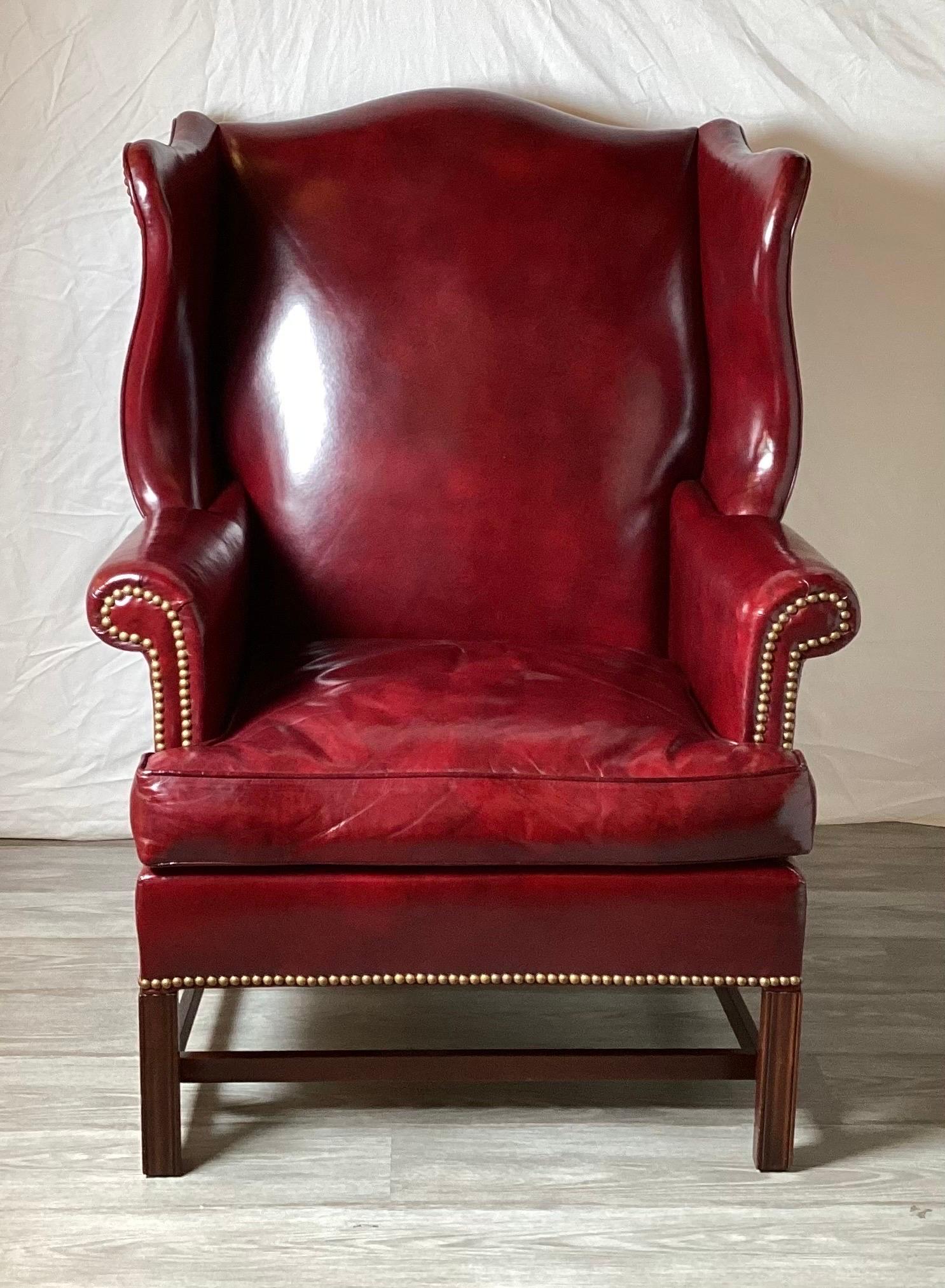 A pair of Classic and shapely cordovan leather wing chairs with brass nail head trim. The sturdy kiln dried hardwood frames with 8 way hand tied springs with a mahogany finished leg. Made exclusively for one of the top furniture retailers in