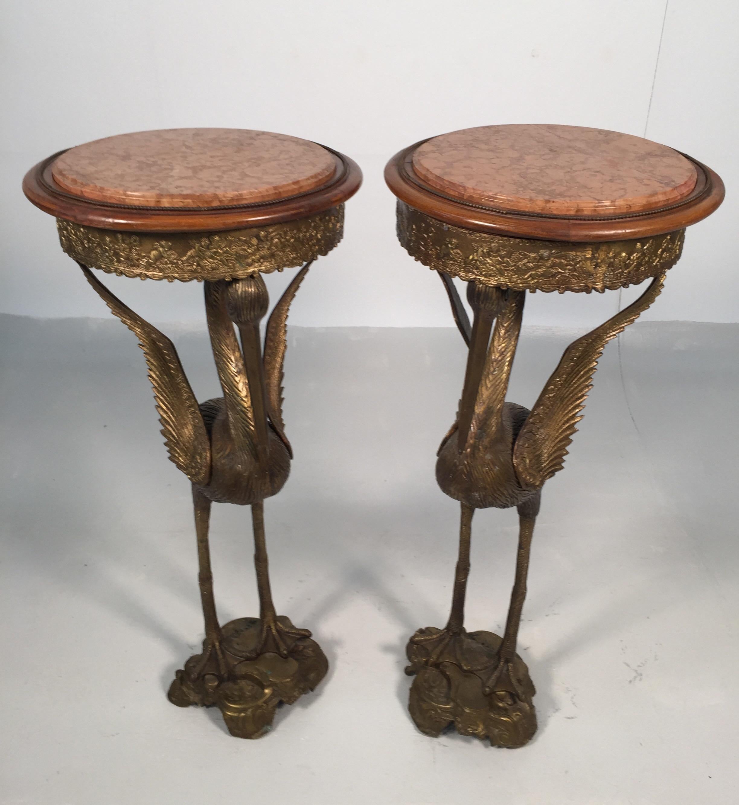 A pair of aesthetic bronze and marble crane motif pedestal, early 1900s. Each with a rouge marble top insert atop a bronze frieze decorated in relief with putti on waterfowl with pedestal base.