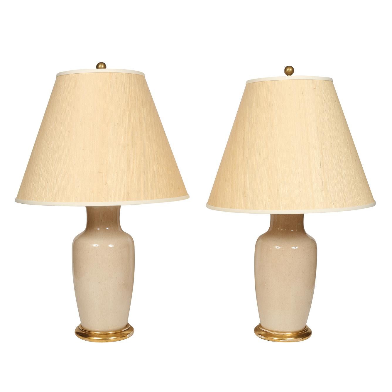A pair of custom cream porcelain lamps with gilt bases.