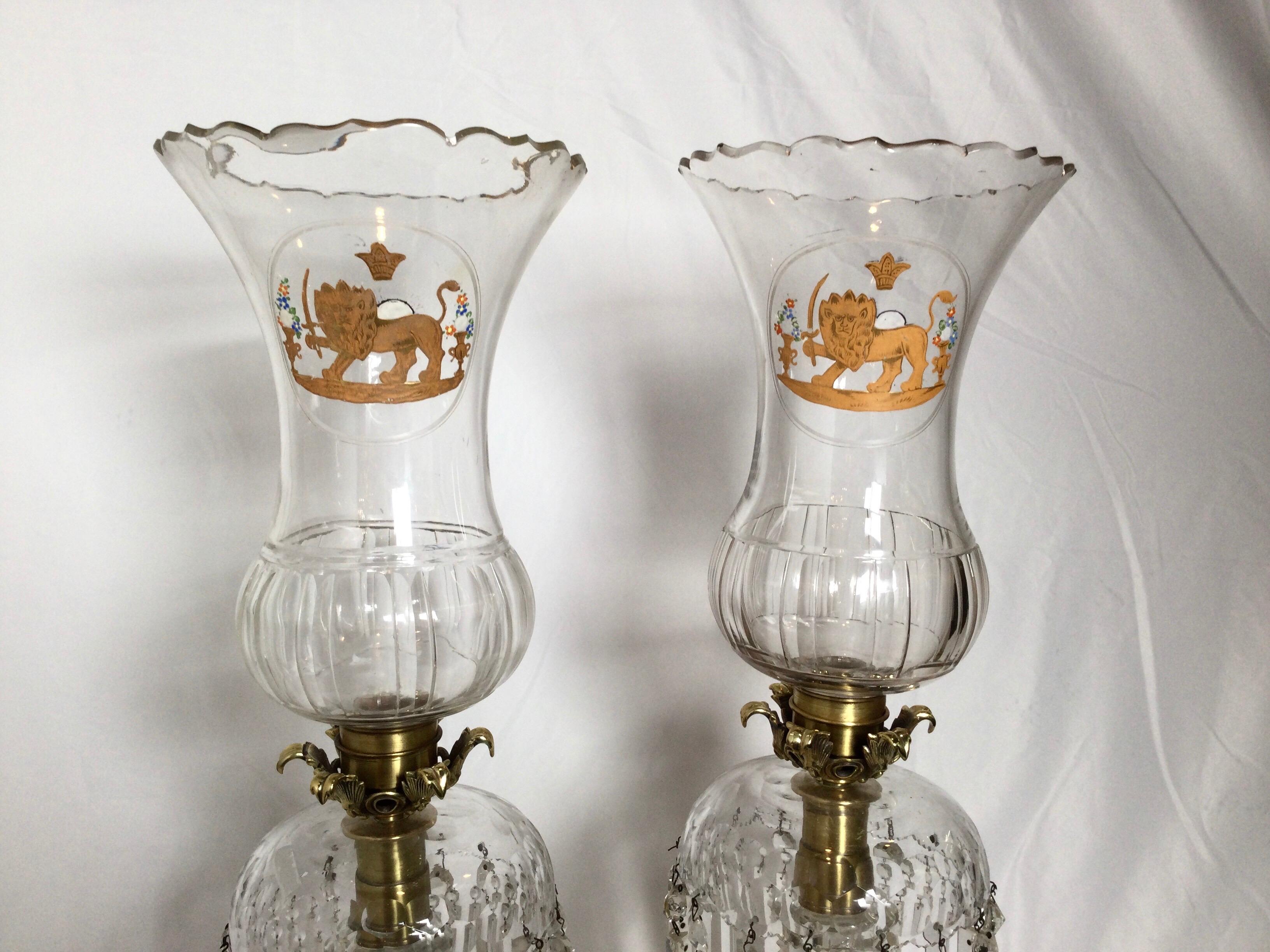 A pair of shapely cut glass hurricane candleholders with a gilt lion emblem on each. The urn form shades with heavy cut and molded bases with long spear tipped crystals.