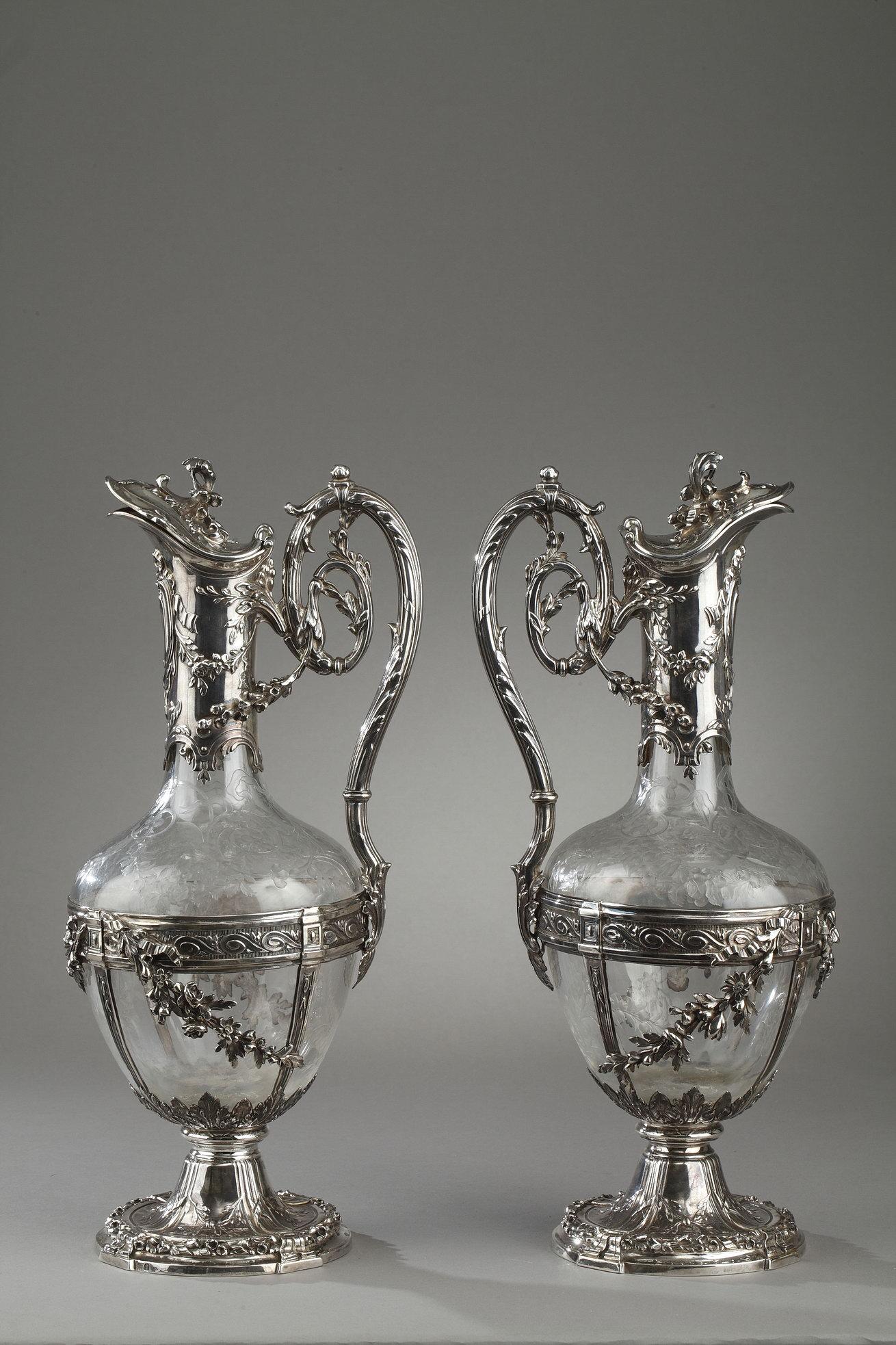 Pair of cut crystal decanter or ewer engraved with scrolls and floral patterns. The crystal is set in a fine silver setting with pilasters and garlands on the body of each carafe. The top and the handle are decorated with floral patterns and a