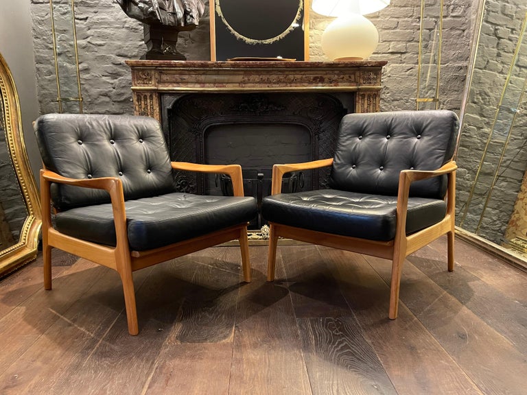 A large and comfortable pair of Scandinavian armchairs/lounge chairs in black leather and cherry wood frames. The cushions buttoned and in great original condition the frames with slated rear rest and shaped and bowed swept armrests. 
In good order