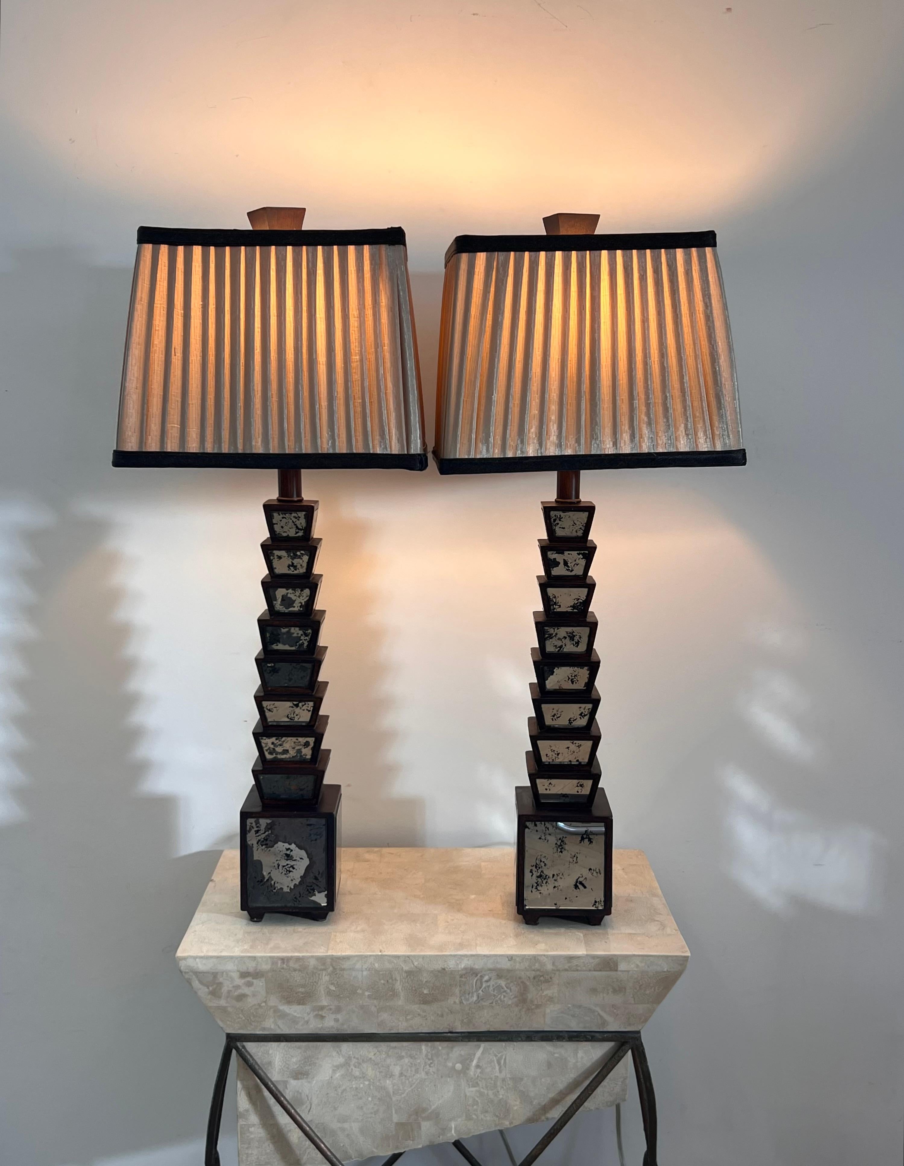 A pair of antique table lamps, circa early 20th century. Featuring graduated wood bases punctuated by patina’d mirror, topped by pleated raw silk shades, this stunning pair is at once elegant and statement, with a foot firmly in the geometrics of
