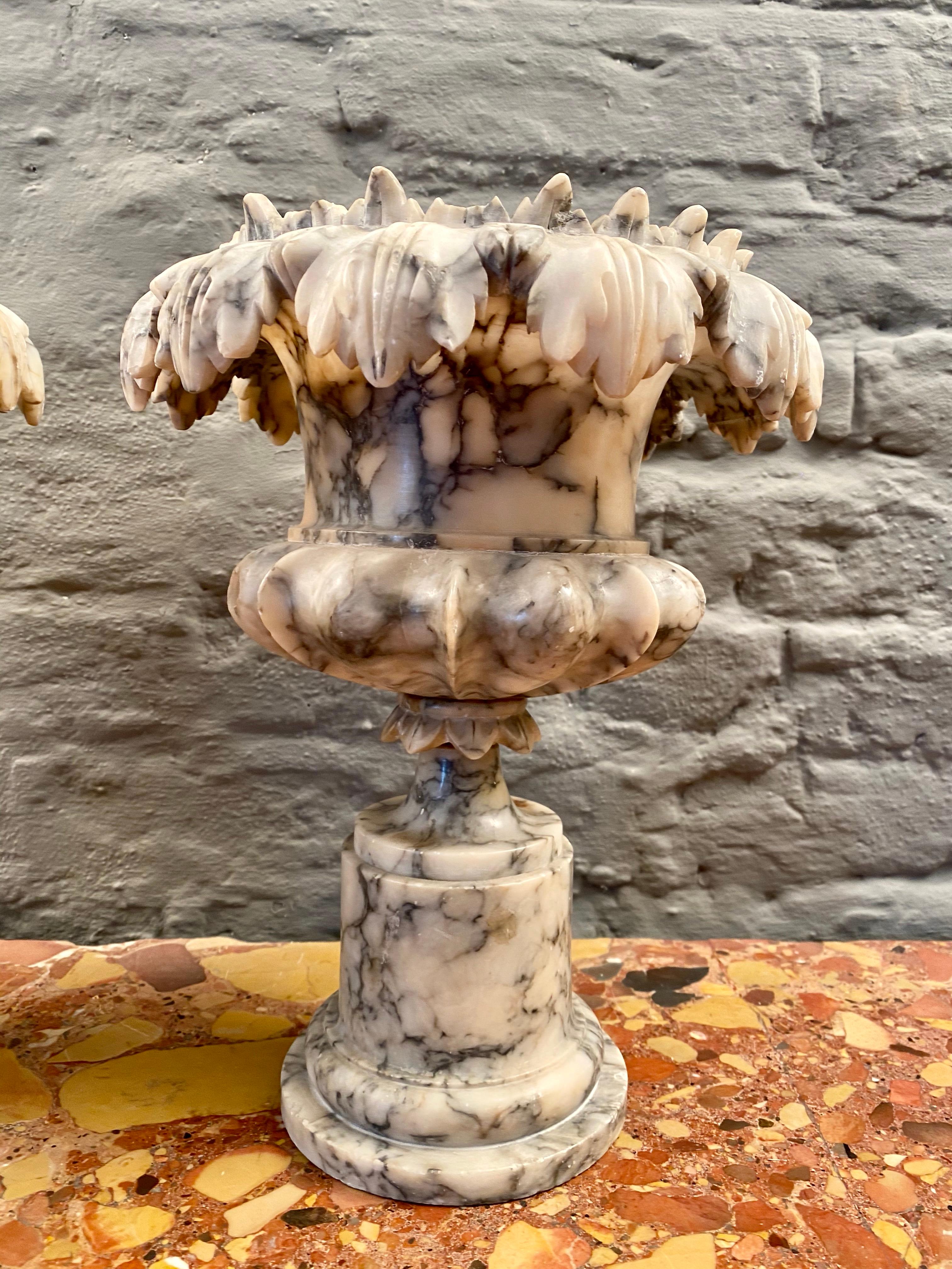 A pair of decorative carved Alabaster urns late 19th or early 20th century. Standing on circular plinth and socles with carved Acanthus edge. Some minor nibbles and one old repair to one of the leafs all shown in images.