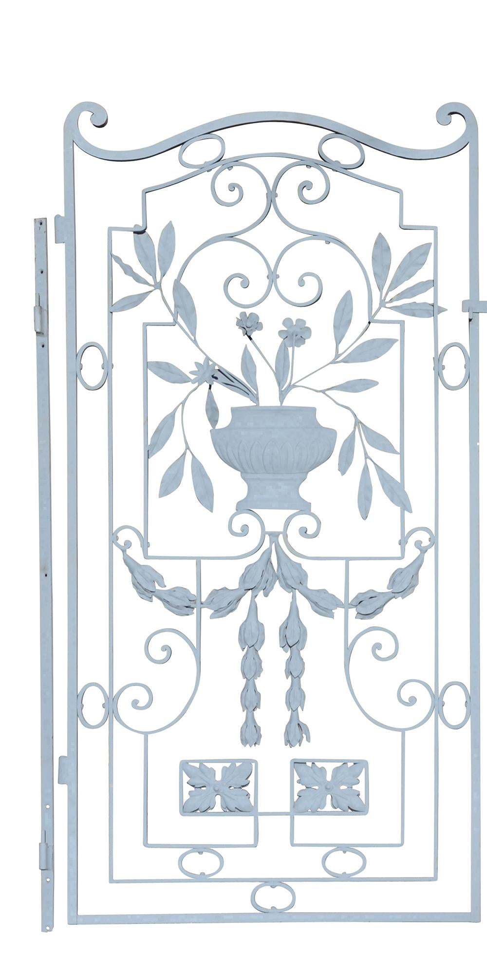 A pair of French iron and toll work garden gates having scroll work embellished with toll work swags and urn with flowers and foliage.