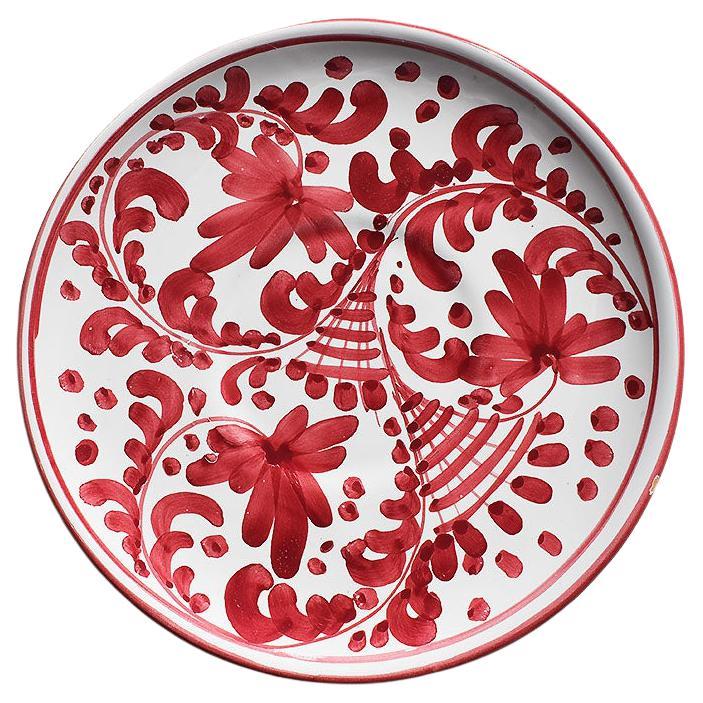 A pair of beautiful ceramic hand-painted plates made in Italy. Italian folk pottery has become highly coveted in recent years. This pair features hand-painted red, pink, and black floral designs on white backgrounds. The rims are accented in red.