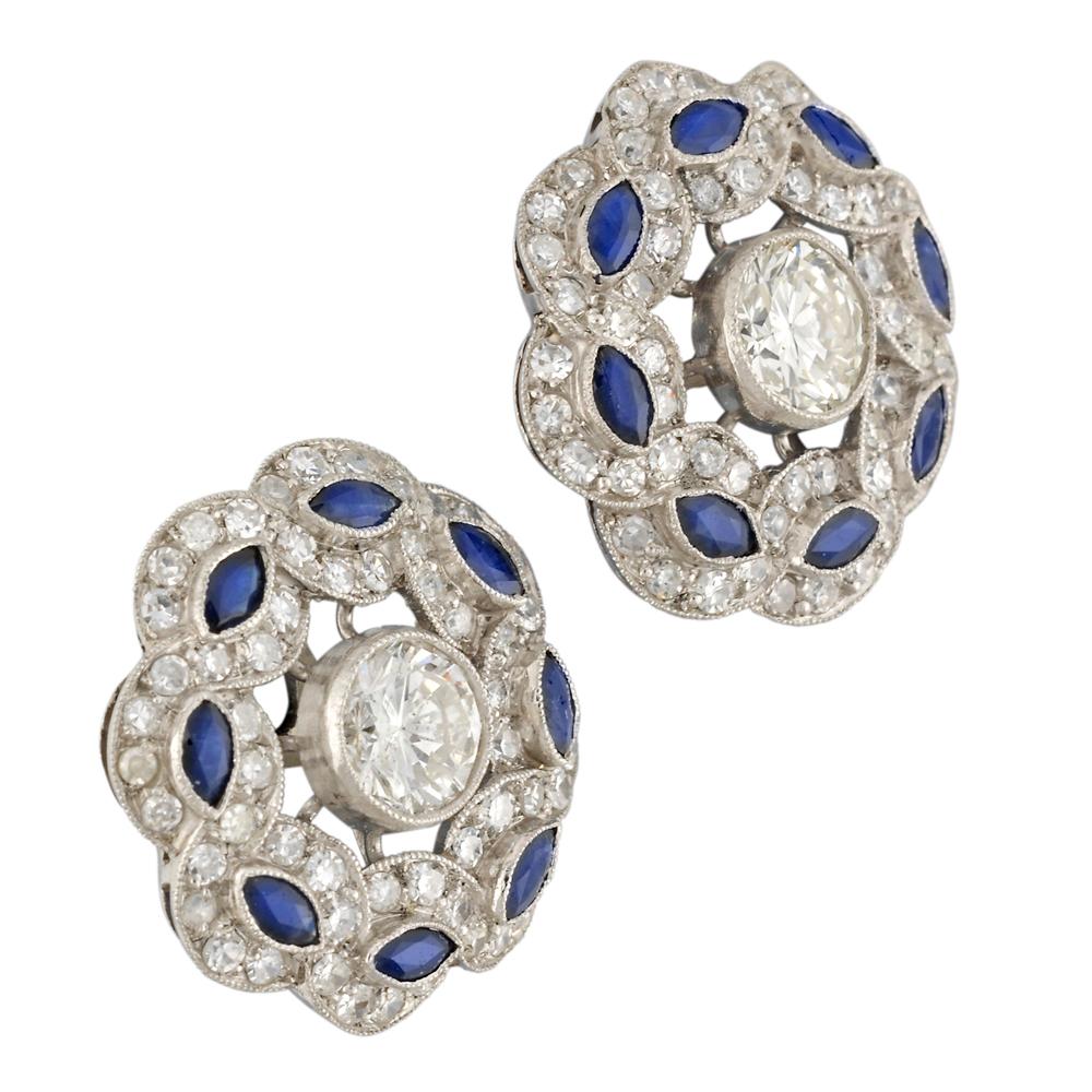 A pair of diamond and sapphire cluster earrings, each earring centrally-set with a round brilliant-cut diamond estimated to weigh 0.5 carats, surrounded by a border of two swiss-cut diamond-set rows entwined around eight marquise-cut sapphires, the