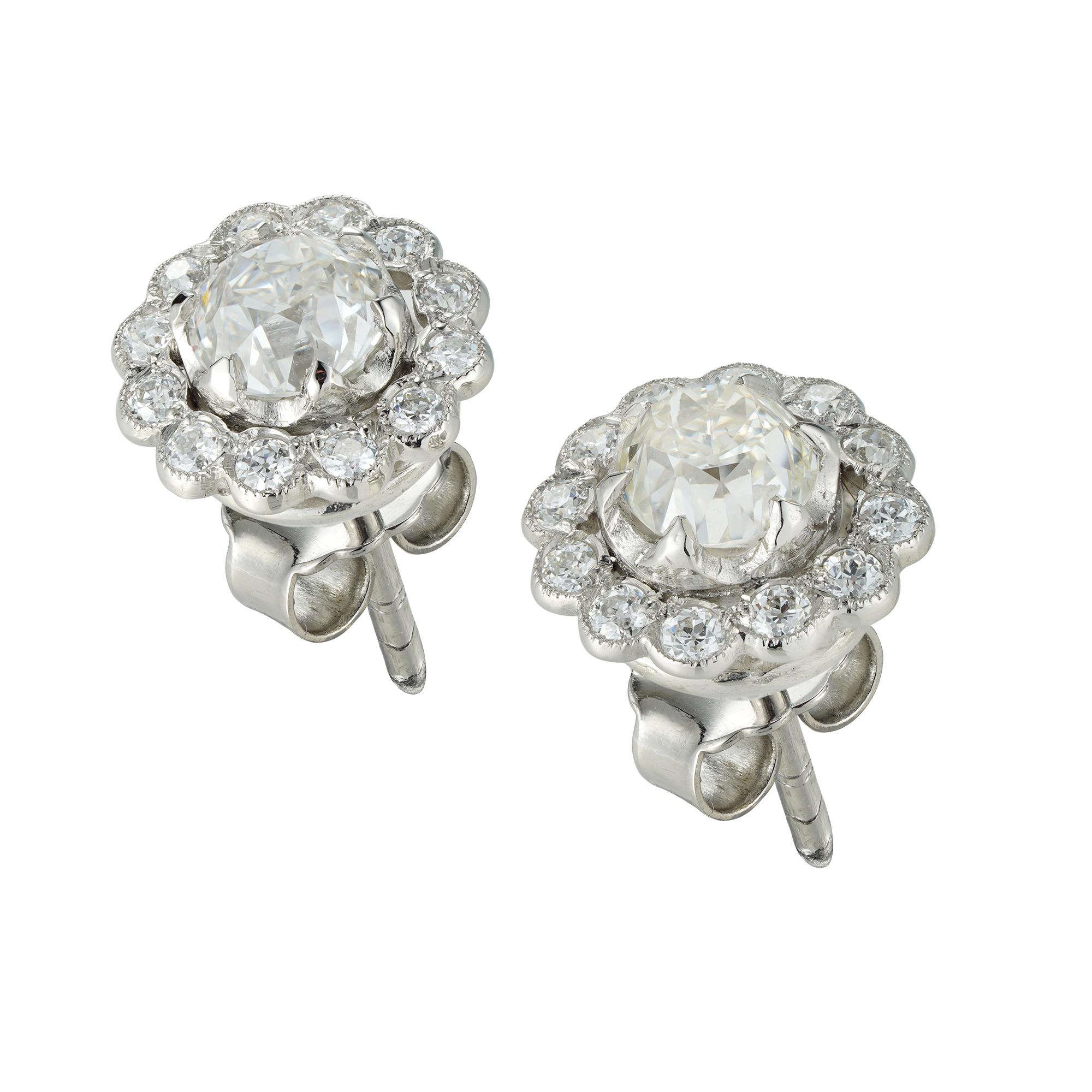 A pair of diamond cluster earrings, the central old brilliant-cut diamonds weighing 1.23 carats, each surrounded by twelve tiny round brilliant-cut diamonds, weighing a further total of 0.25cts, claw and millegrain set in platinum mount, with post
