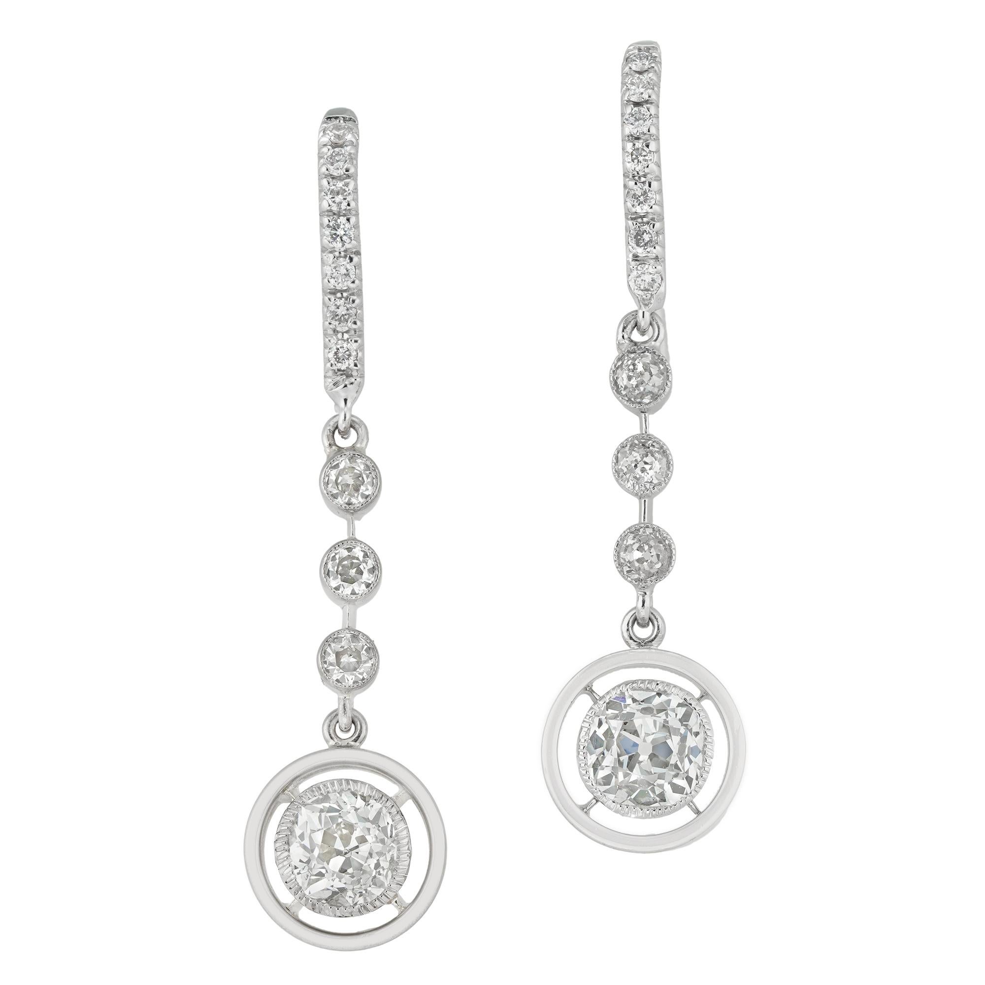 A pair of diamond drop earrings, each earring with an old-cut diamond estimated to weigh 0.65 carats milligram-set in platinum collet and surrounded by a circular frame with day-light in between, suspended by a run of three small old-cut diamonds