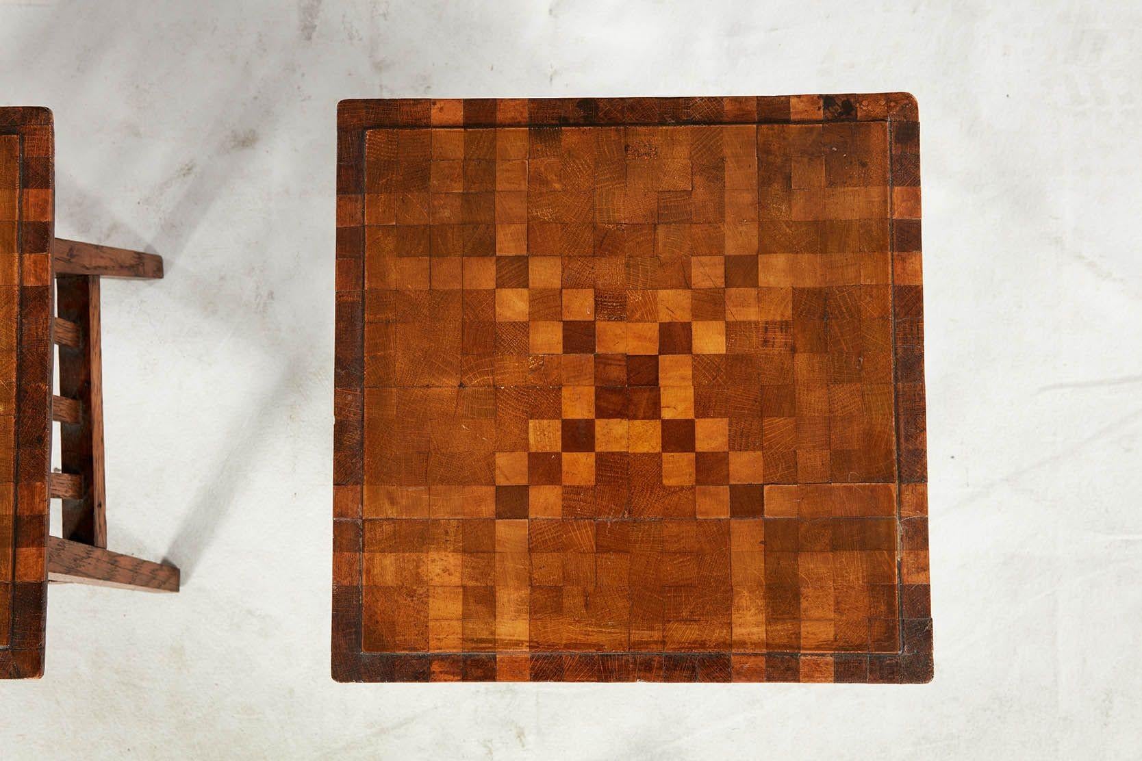 A pair of diminutive tables with geometric chequered tops of graduated colored squares, with molded edges, on fenced aprons and splayed legs. Useful as drinks tables or book stools.